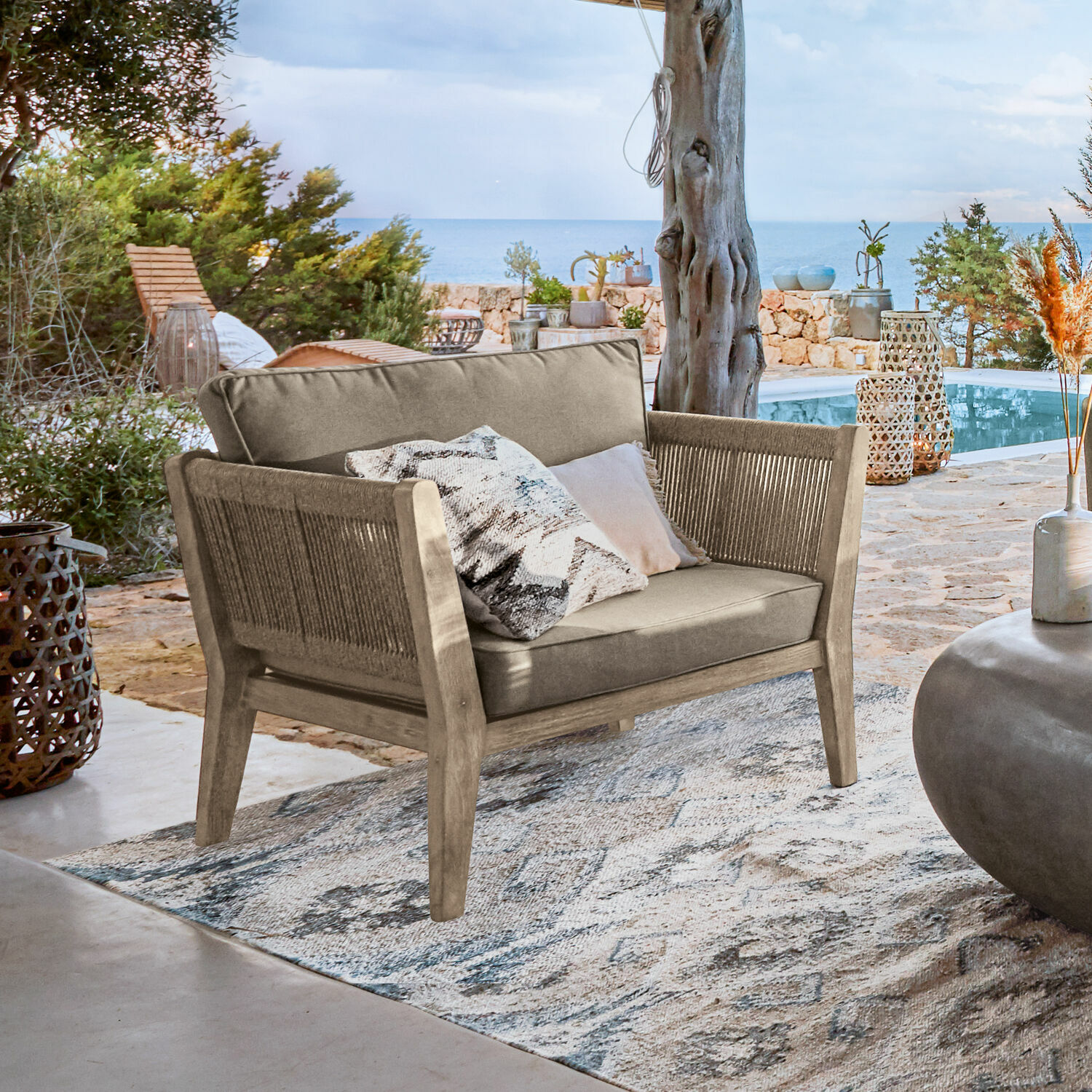 Sofá de exterior de madera y tela beige en terraza con vista al mar