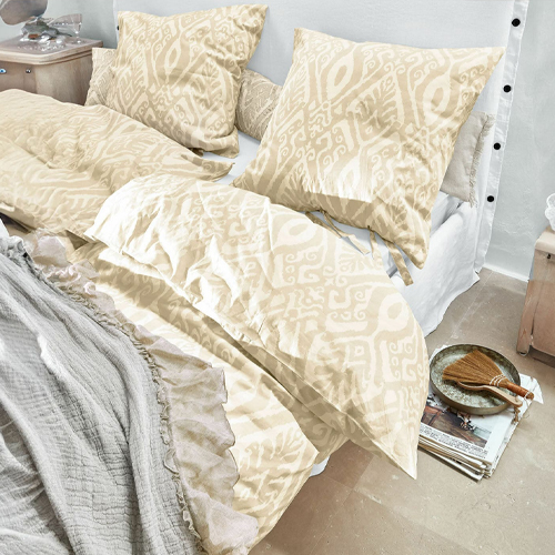 Ropa de cama beige con patrón geométrico de tela suave sobre cama en habitación luminosa