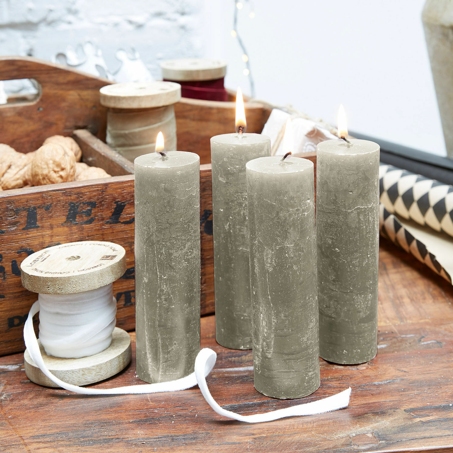 Set de 4 velas Muriel Cuatro velas cilíndricas grises sobre mesa de madera con carrete de madera y decoraciones