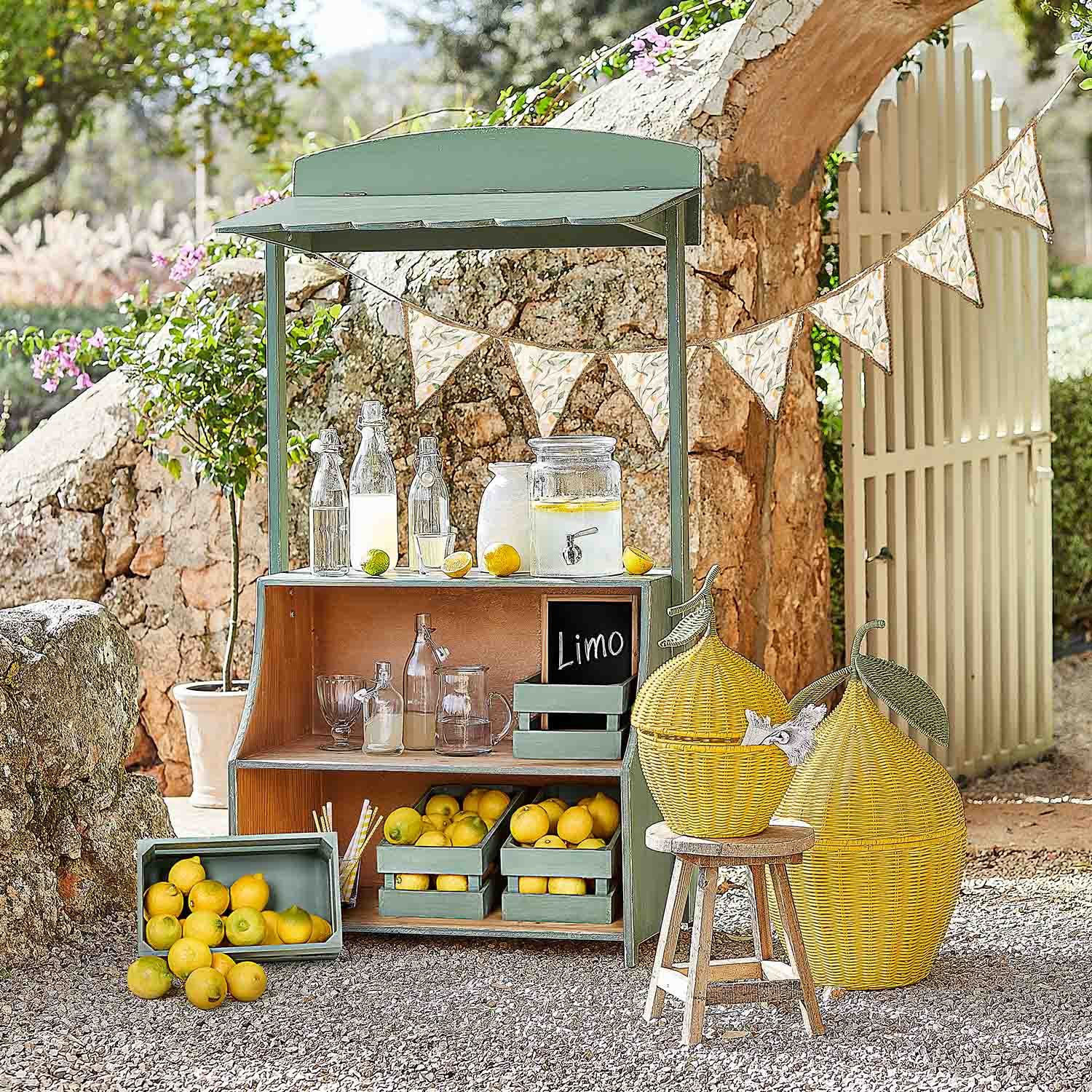 Puesto de madera verde con limones y botellas de vidrio para limonada en jardín soleado