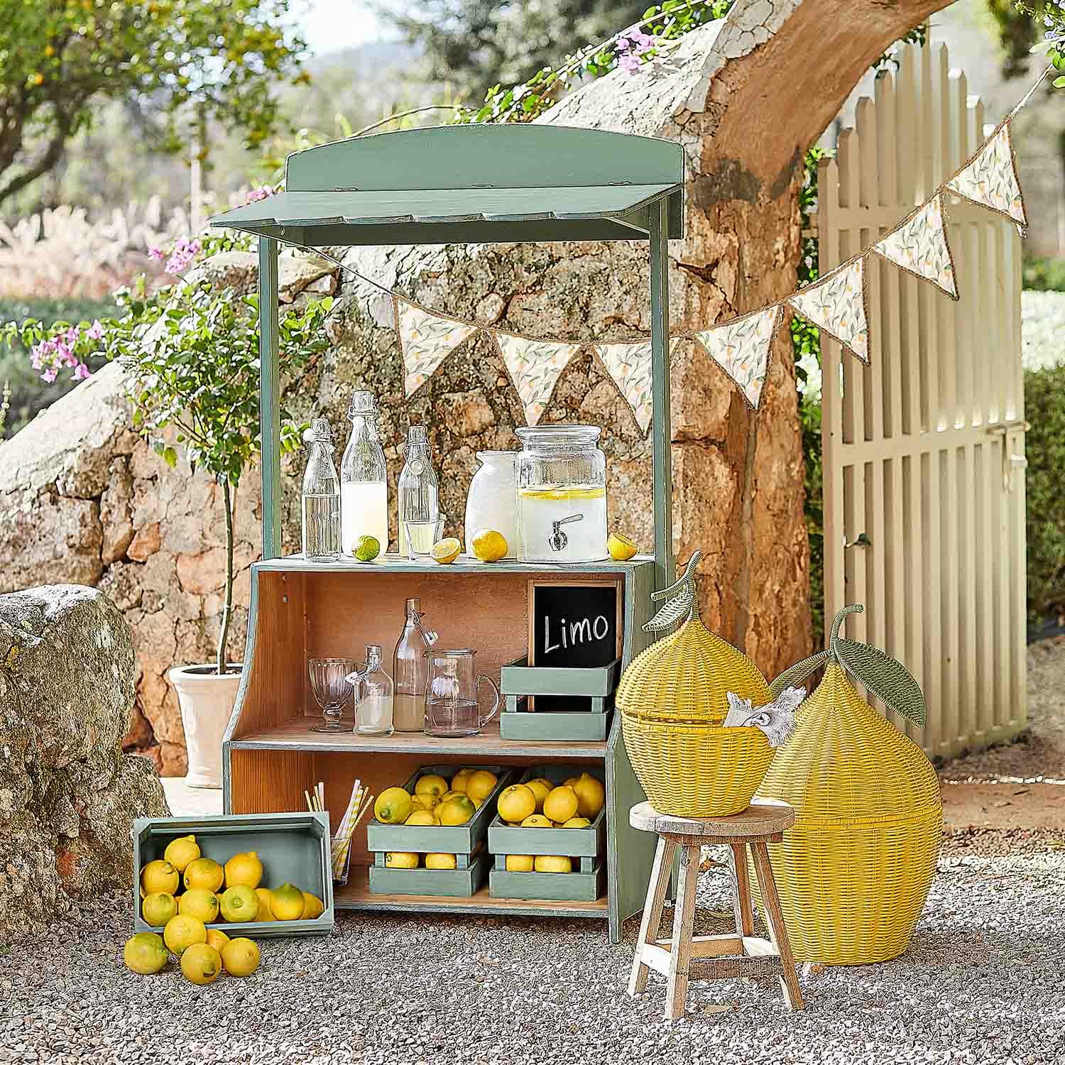 Puesto de madera verde con limones y botellas de vidrio para limonada en jardín soleado