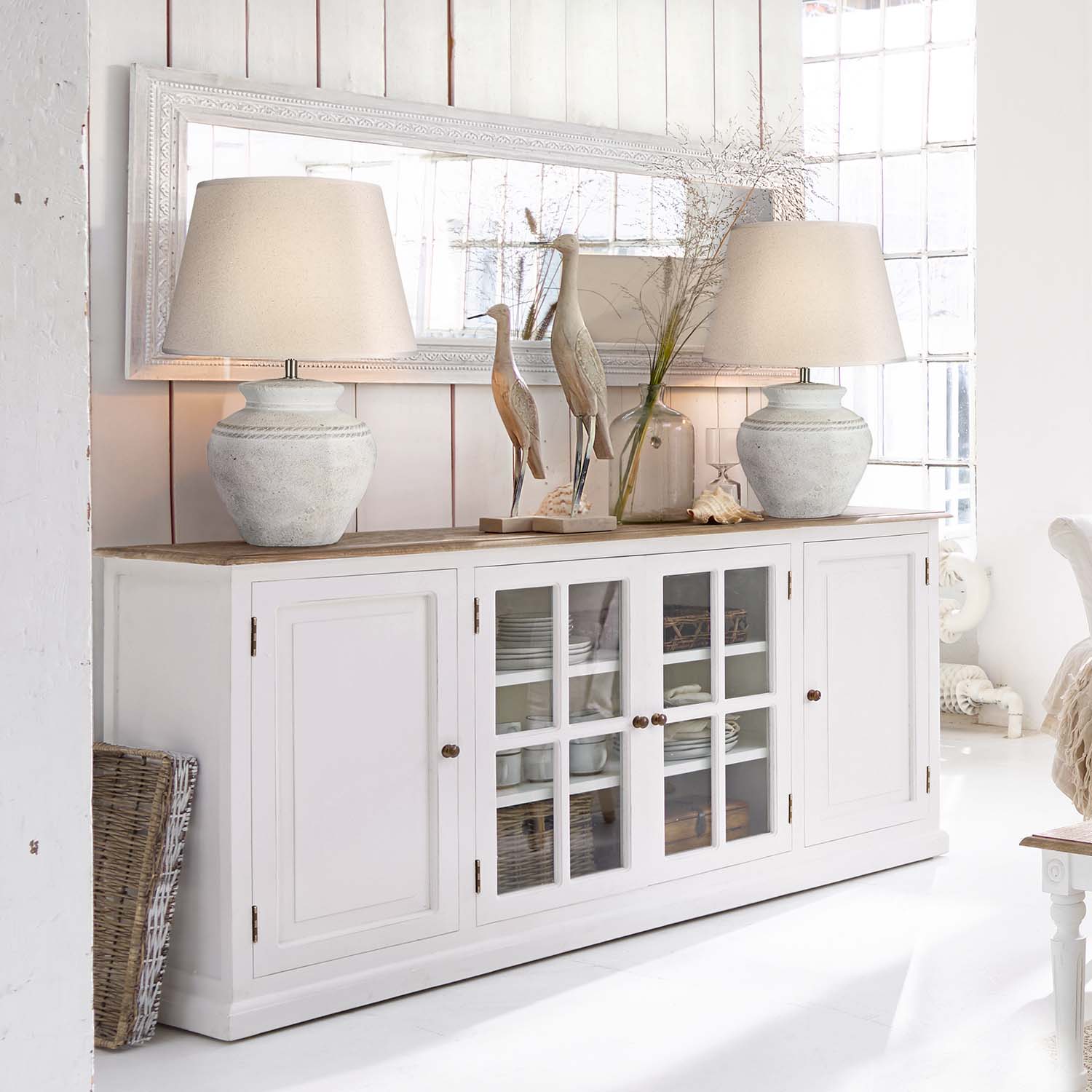 Aparador de madera blanca con puertas de cristal y lámparas de cerámica en interior luminoso