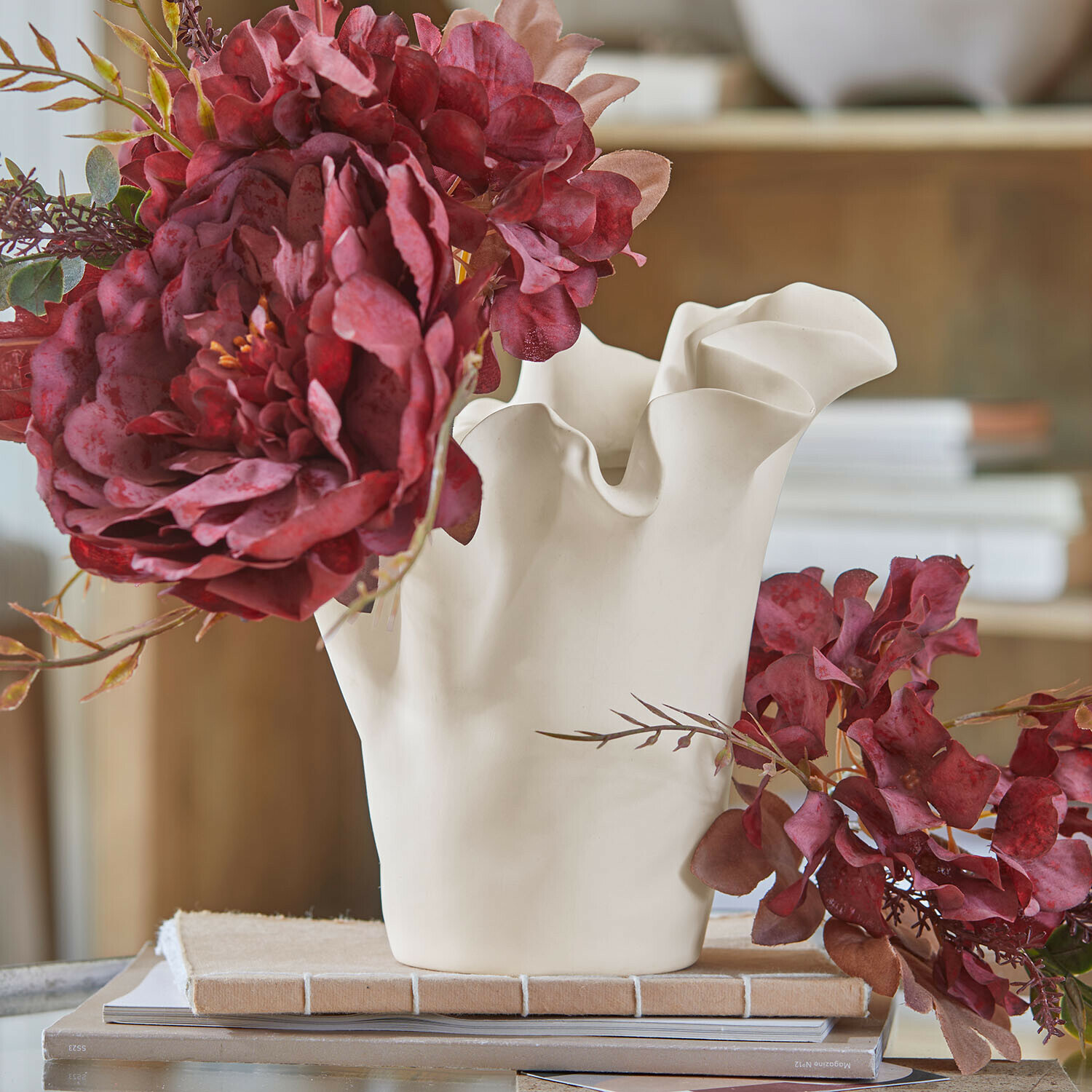 Jarrón Elvessa Jarrón de cerámica blanca con borde ondulado y flores artificiales rojas sobre mesa con libros