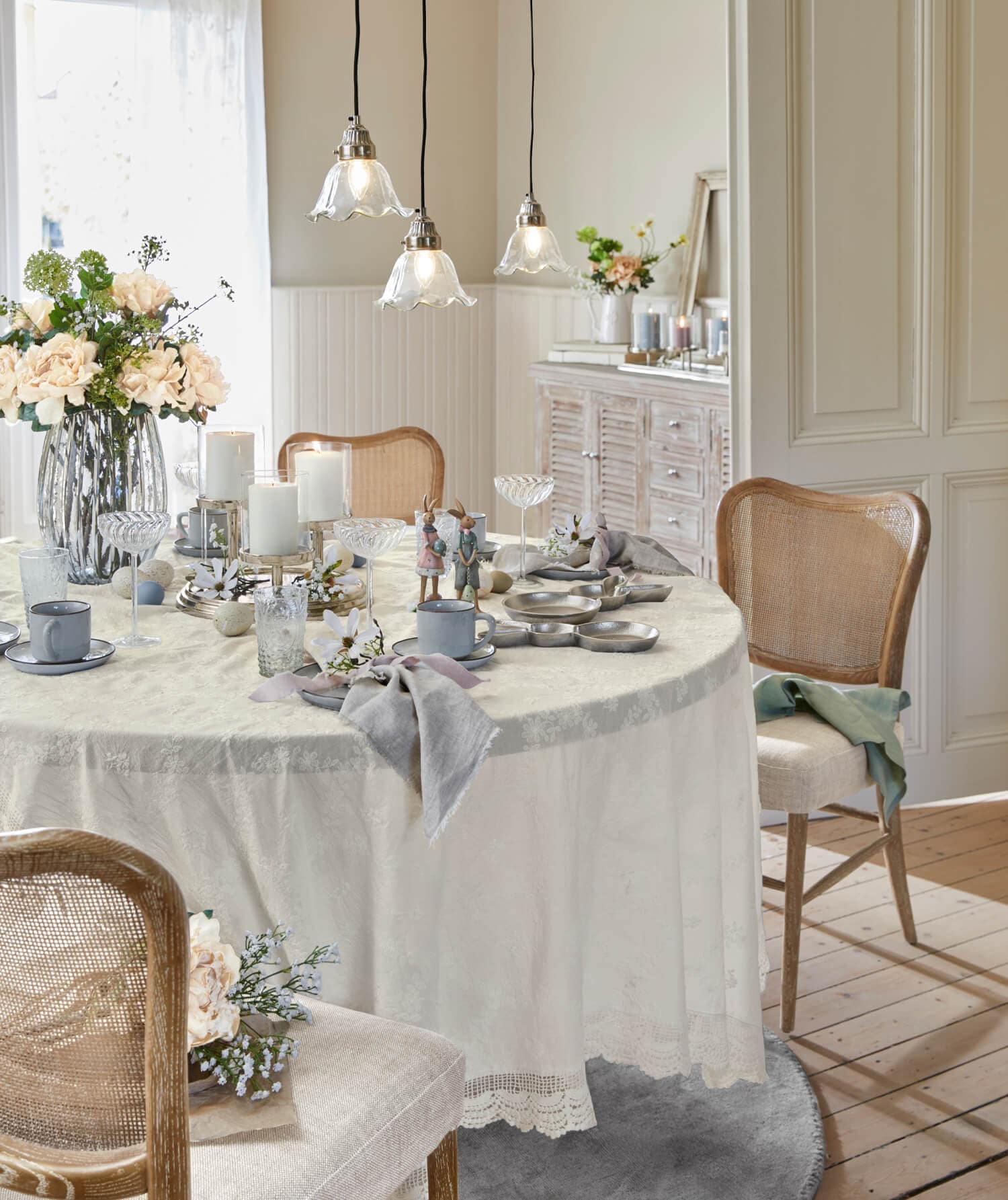 Mesa clara con mantel crema y decoración rústica, sillas de madera y flores en comedor luminoso