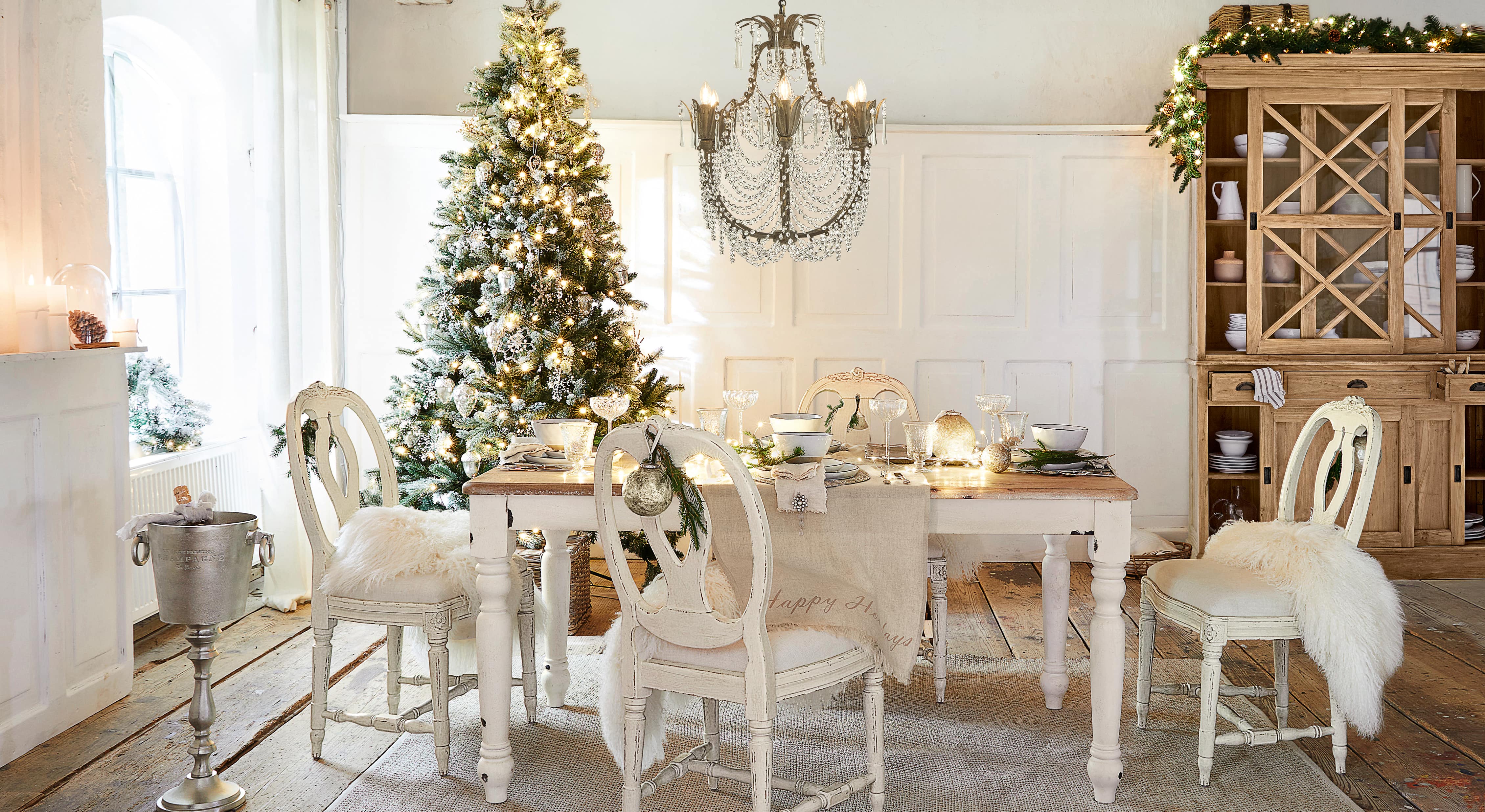 Comedor con mesa y sillas blancas de madera, decorado para Navidad con árbol y lámpara de cristal