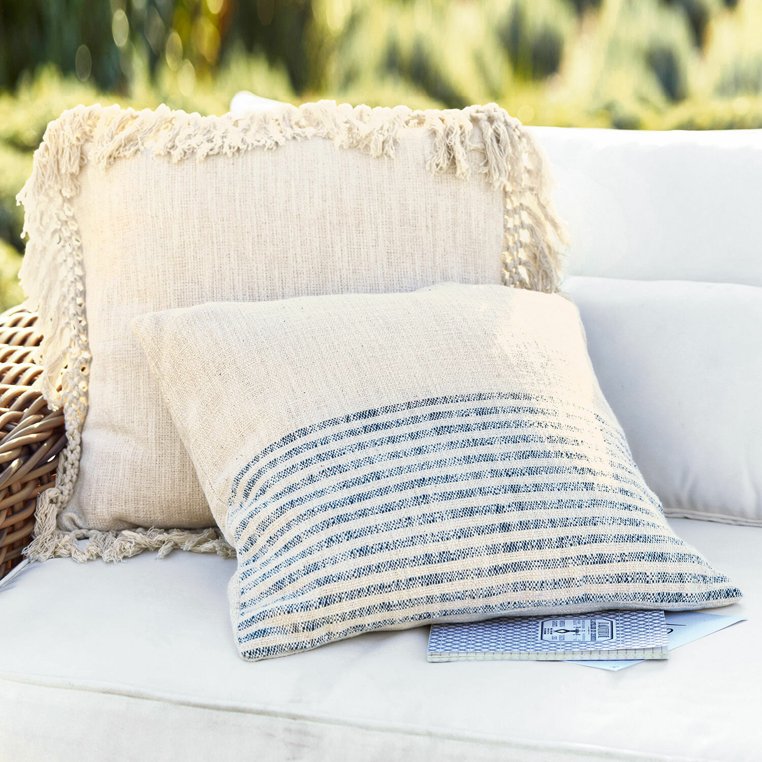 Set de 2 fundas de cojín Marpent Cojines decorativos de lino beige con flecos y rayas sobre sofá blanco al aire libre