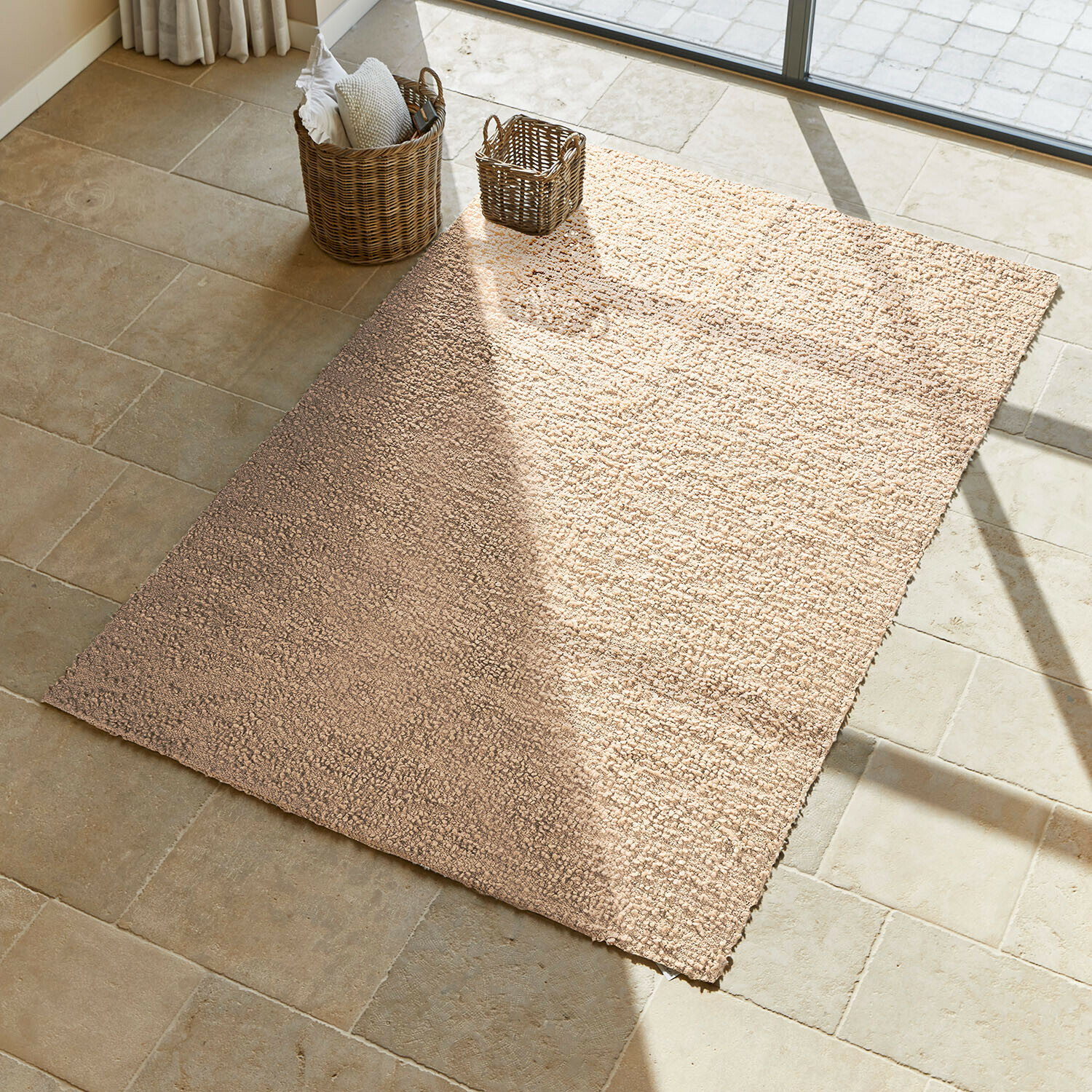 Alfombra Wodaha Alfombra beige de material suave sobre suelo de piedra clara con cestas de mimbre al lado