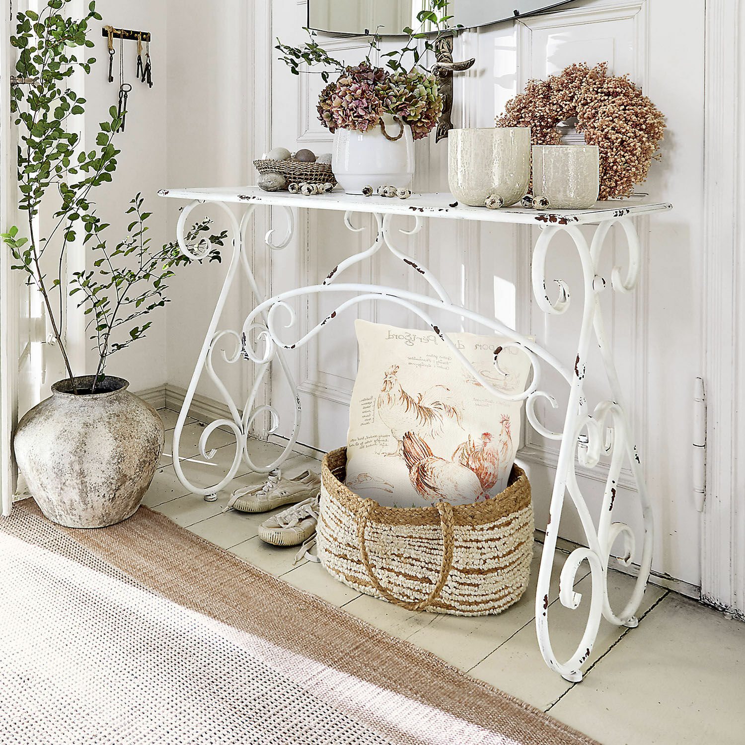 Consola Stonem Mesa metálica blanca con plantas decorativas y cesta de mimbre con cojín en estilo rústico