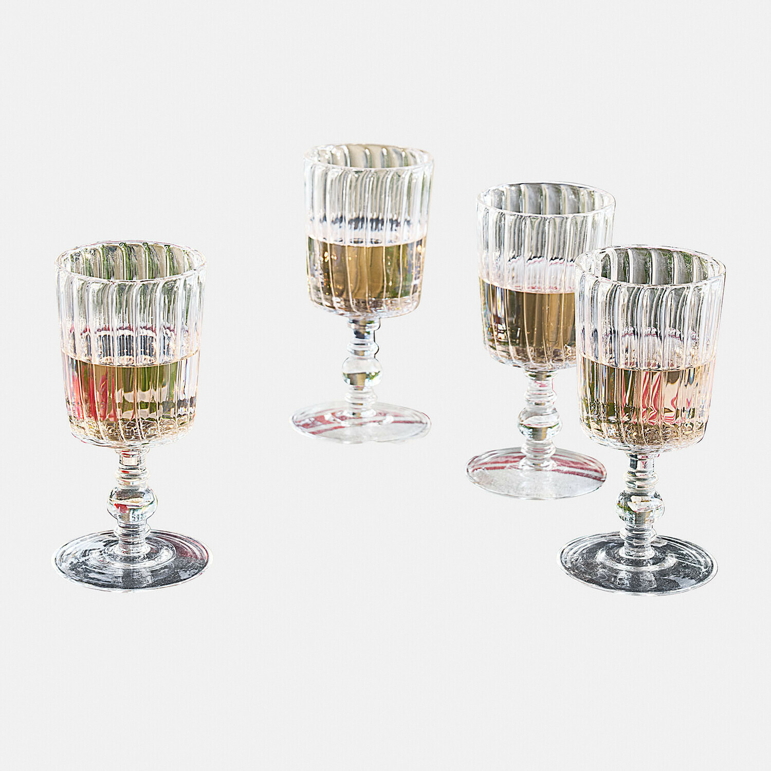 Conjunto de cuatro copas transparentes de vidrio estriado con bebida clara, copas de vino elegantes
