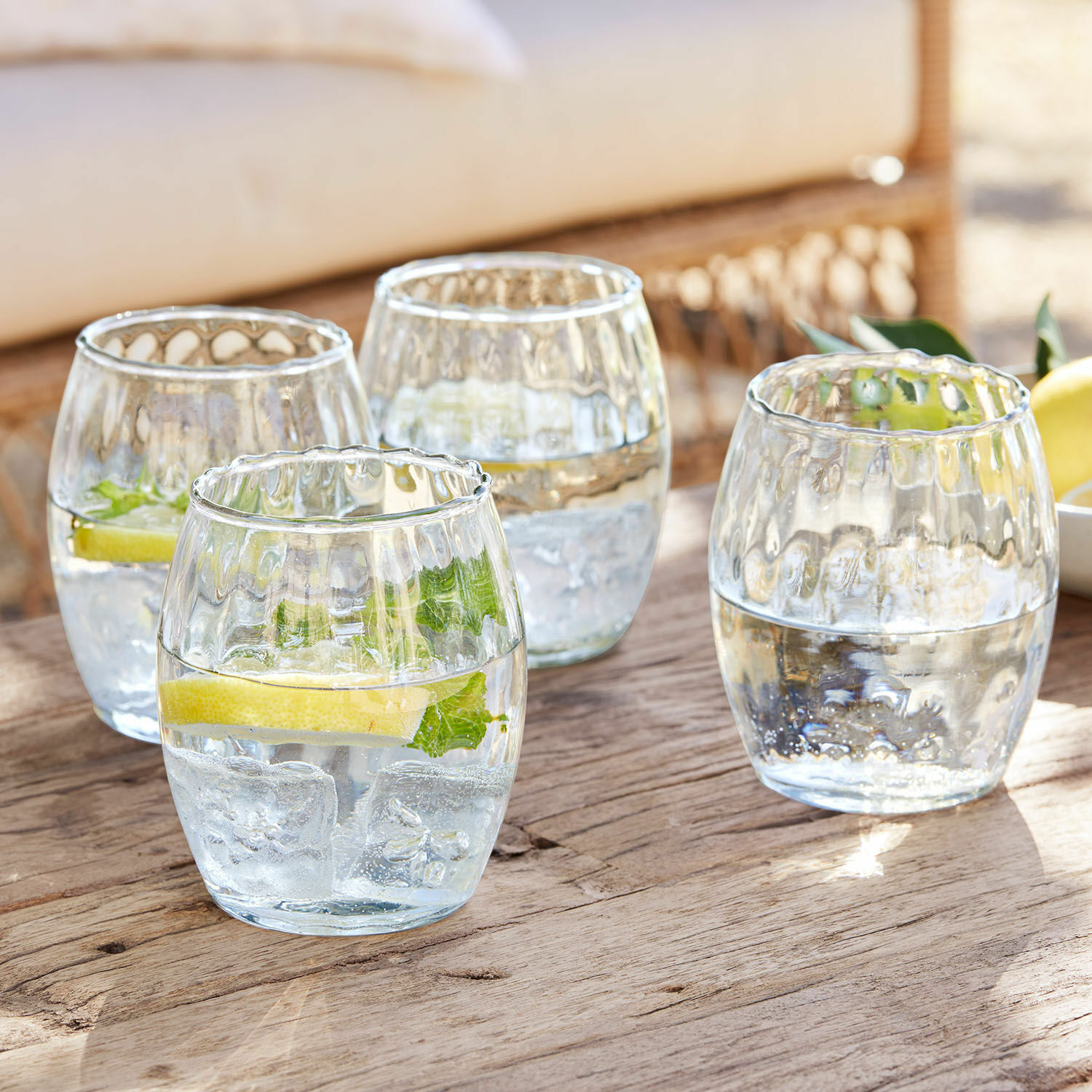 Set de 4 vasos Bourgavin Conjunto de cuatro vasos de vidrio transparente con agua, hielo y limón sobre mesa de madera