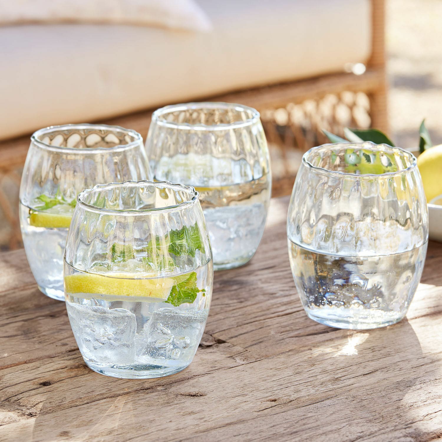 Set de 4 vasos Bourgavin Conjunto de cuatro vasos de vidrio transparente con agua, hielo y limón sobre mesa de madera