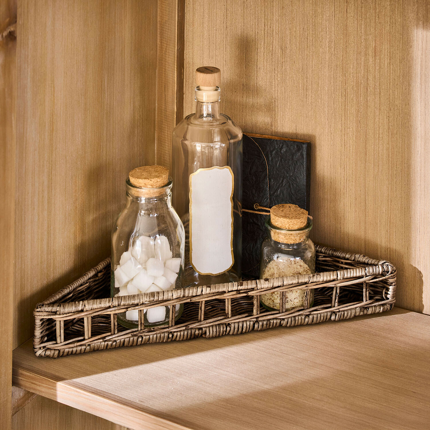 Cesta triangular de ratán natural con tres botellas de vidrio y un cuaderno en estante de madera