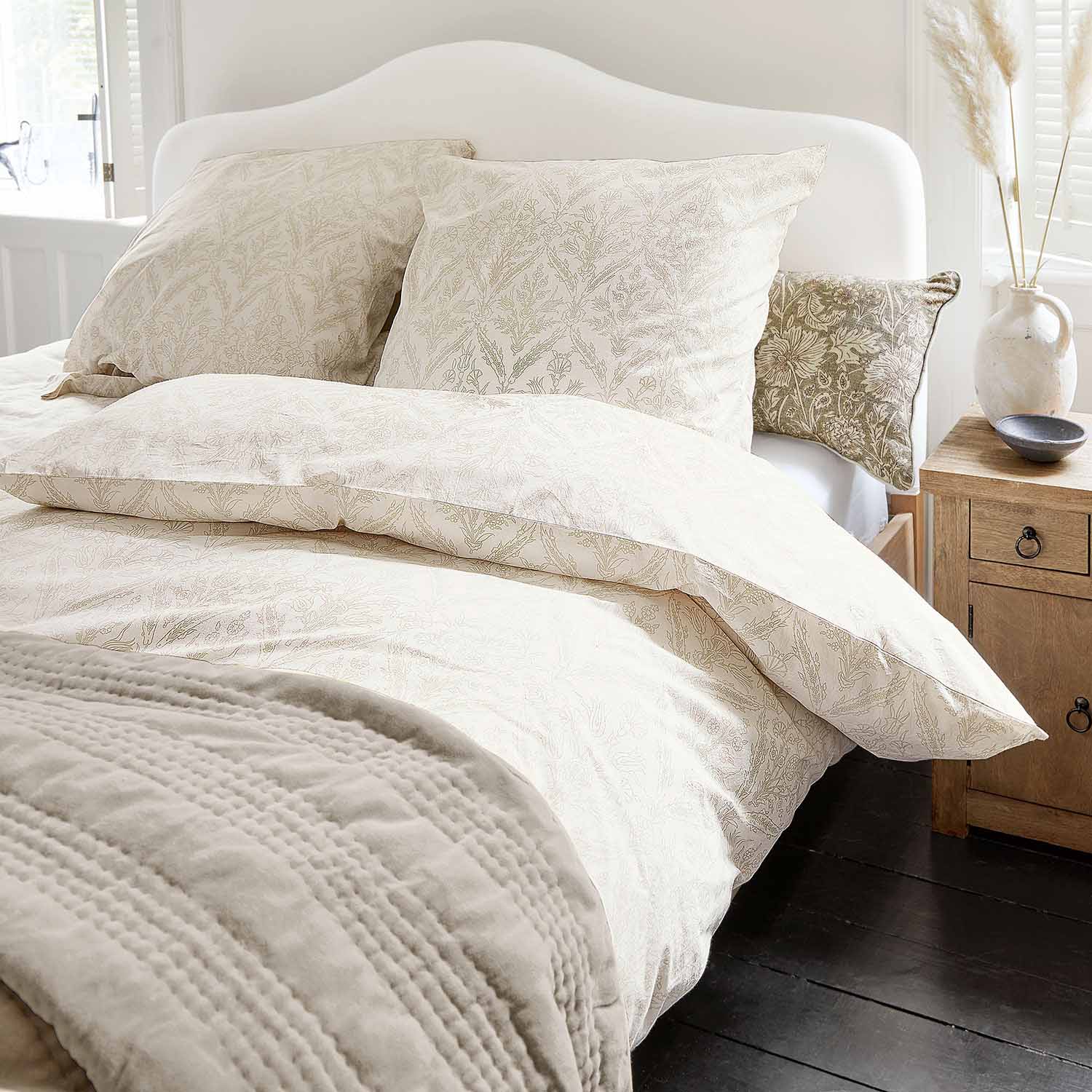 Ropa de cama de algodón clara con delicado estampado vegetal y manta suave en dormitorio acogedor