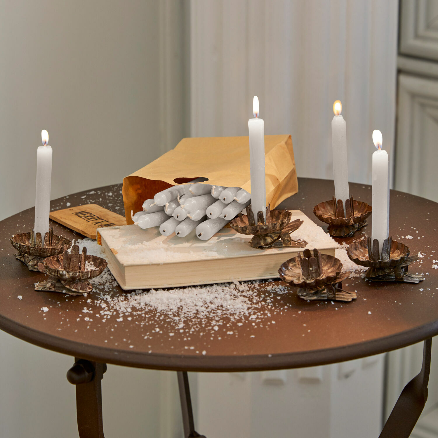 Set de 20 velas Noufa Velas blancas de cera en candelabros de metal cobre sobre mesa marrón con bolsa de papel