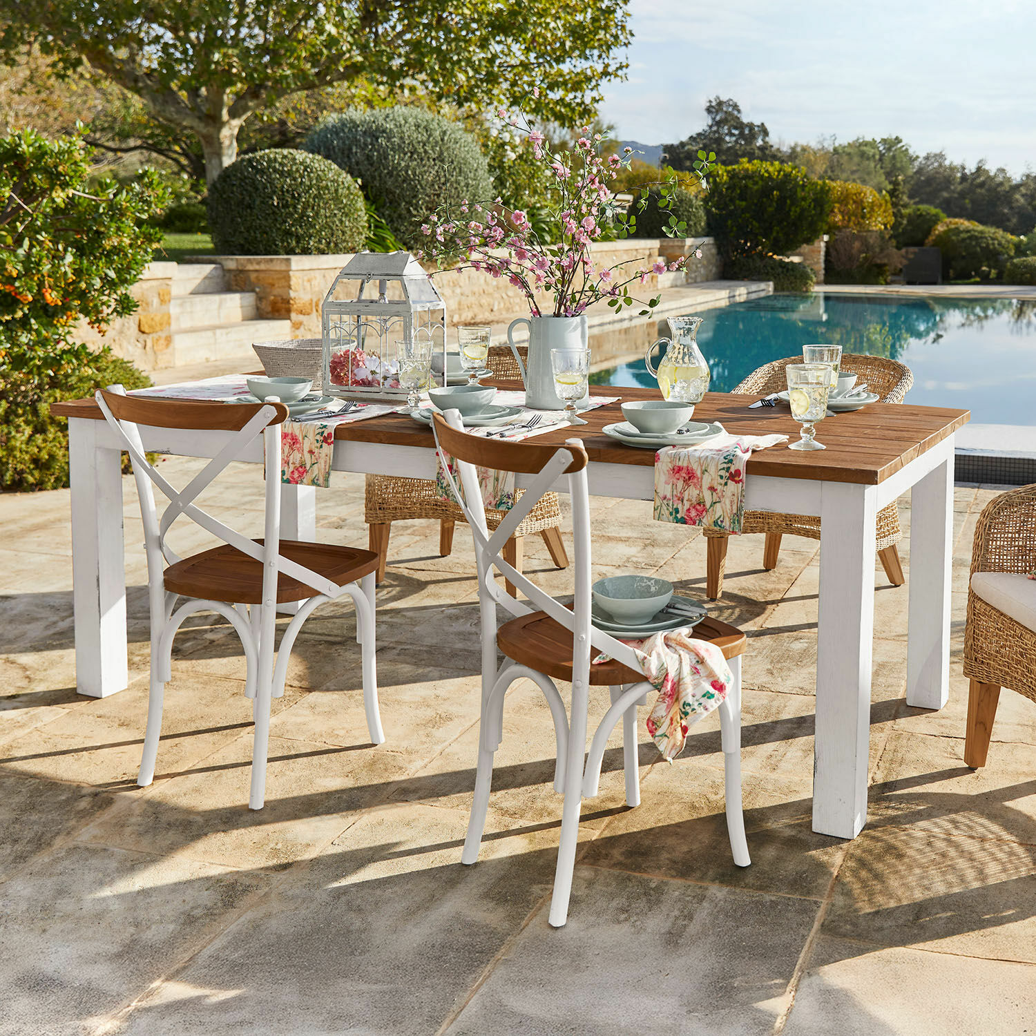 Mesa Kirkdale Mesa de jardín de madera con patas blancas y sillas rústicas junto a la piscina
