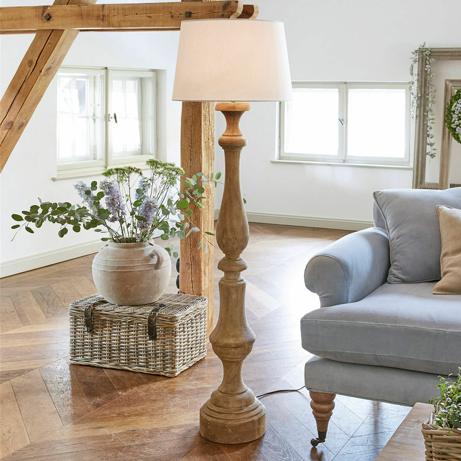 Lámpara de pie Etienne Lámpara de pie de madera con pantalla blanca en sala luminosa con sofá azul y cesta de mimbre