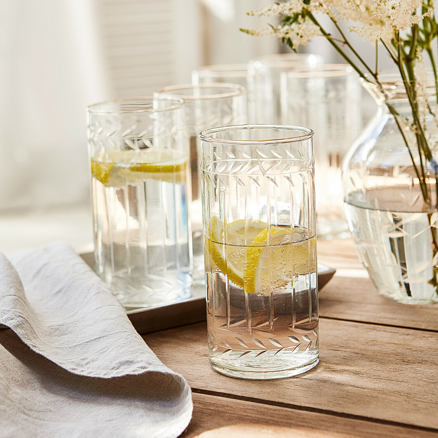 Set de 6 vasos Padiès Vasos de vidrio transparente con diseño grabado de hojas, llenos de agua con limón sobre mesa de madera