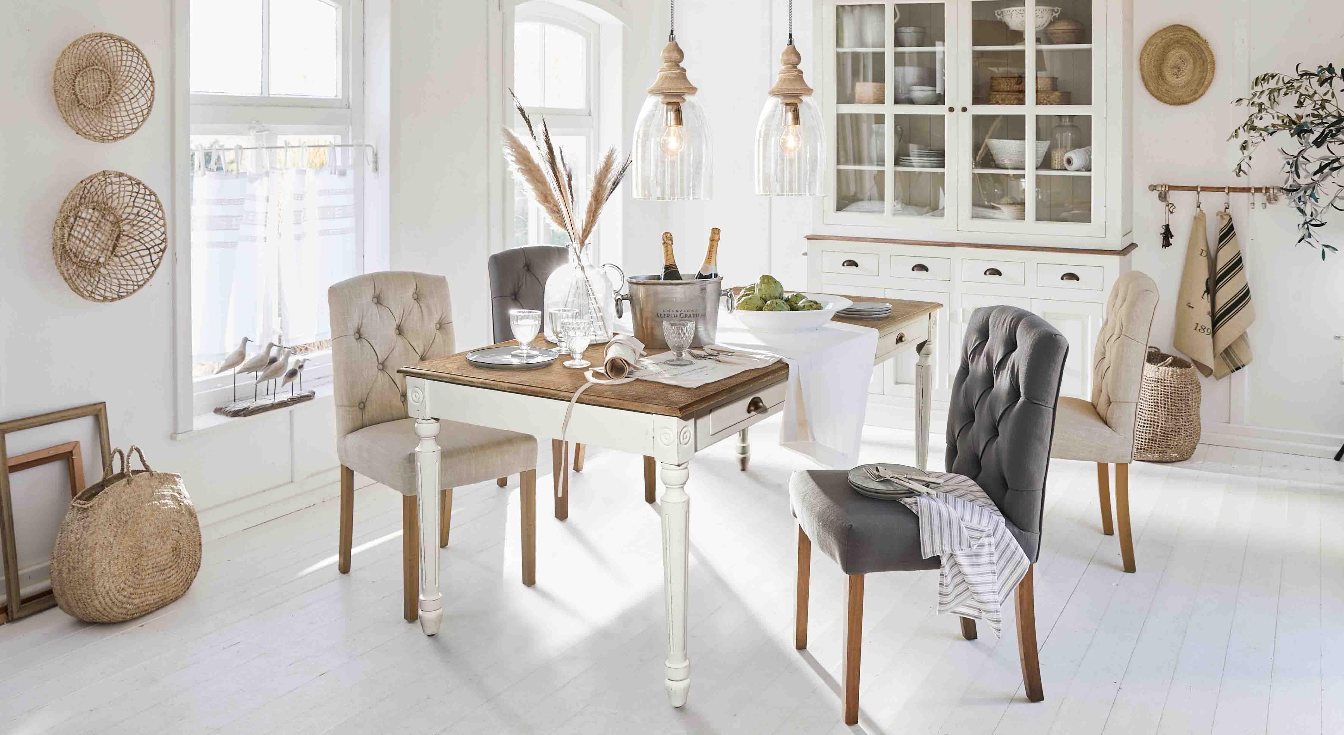 Comedor rústico con mesa de madera blanca y sillas tapizadas en beige y gris en ambiente luminoso