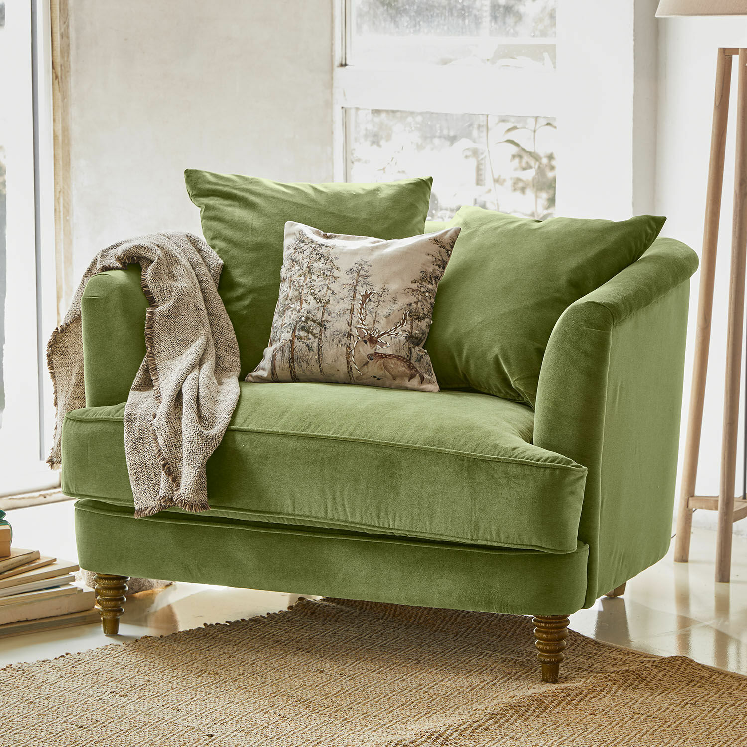 Sillón Etueffont Sofá verde de terciopelo con cojines y manta beige sobre alfombra natural en interior luminoso