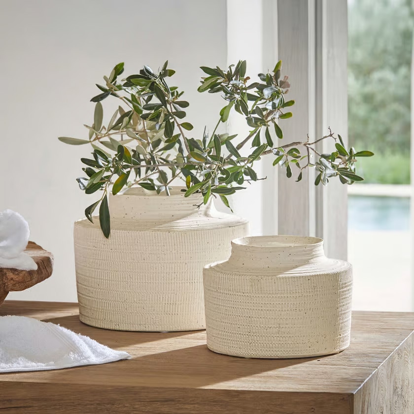 Dos jarrones de cerámica crema con textura sobre mesa de madera con ramas verdes