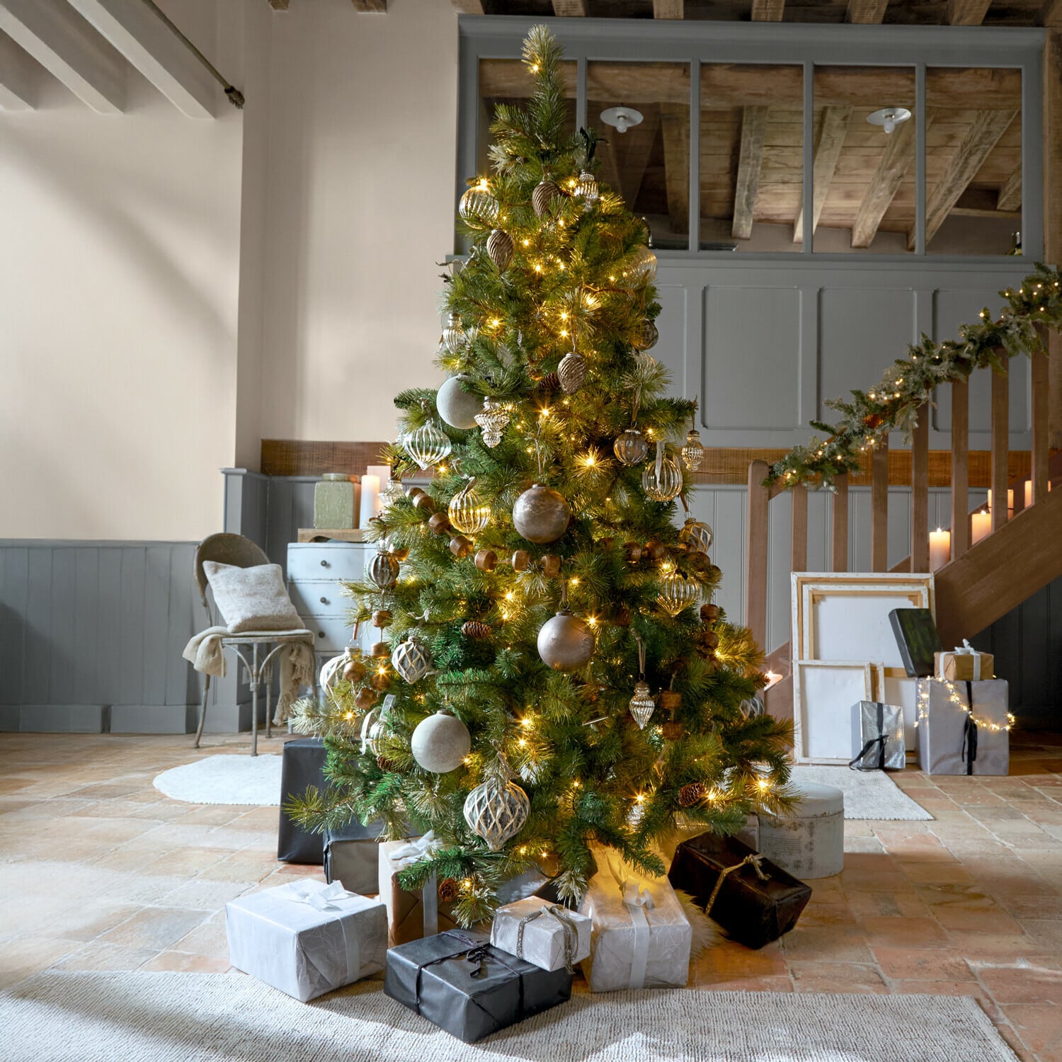 Árbol de Navidad Aure Árbol de Navidad decorado con ramas verdes y luces doradas en interior acogedor con regalos