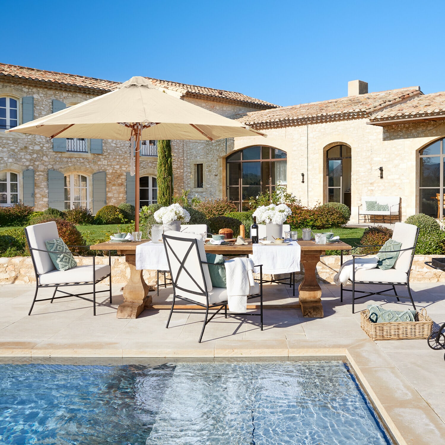 Mesa Devonshire Conjunto de muebles de jardín con sombrilla beige y cojines junto a la piscina frente a casa de piedra