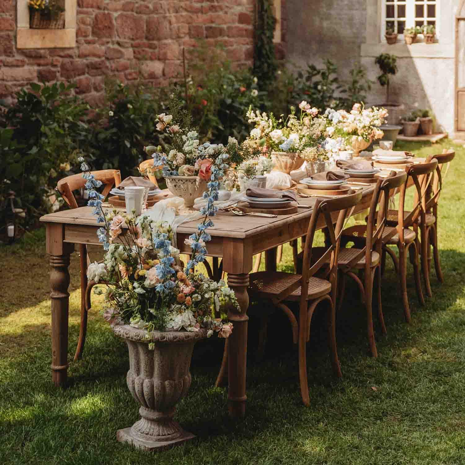 Mesa de madera en jardín con decoración floral y vajilla para evento al aire libre