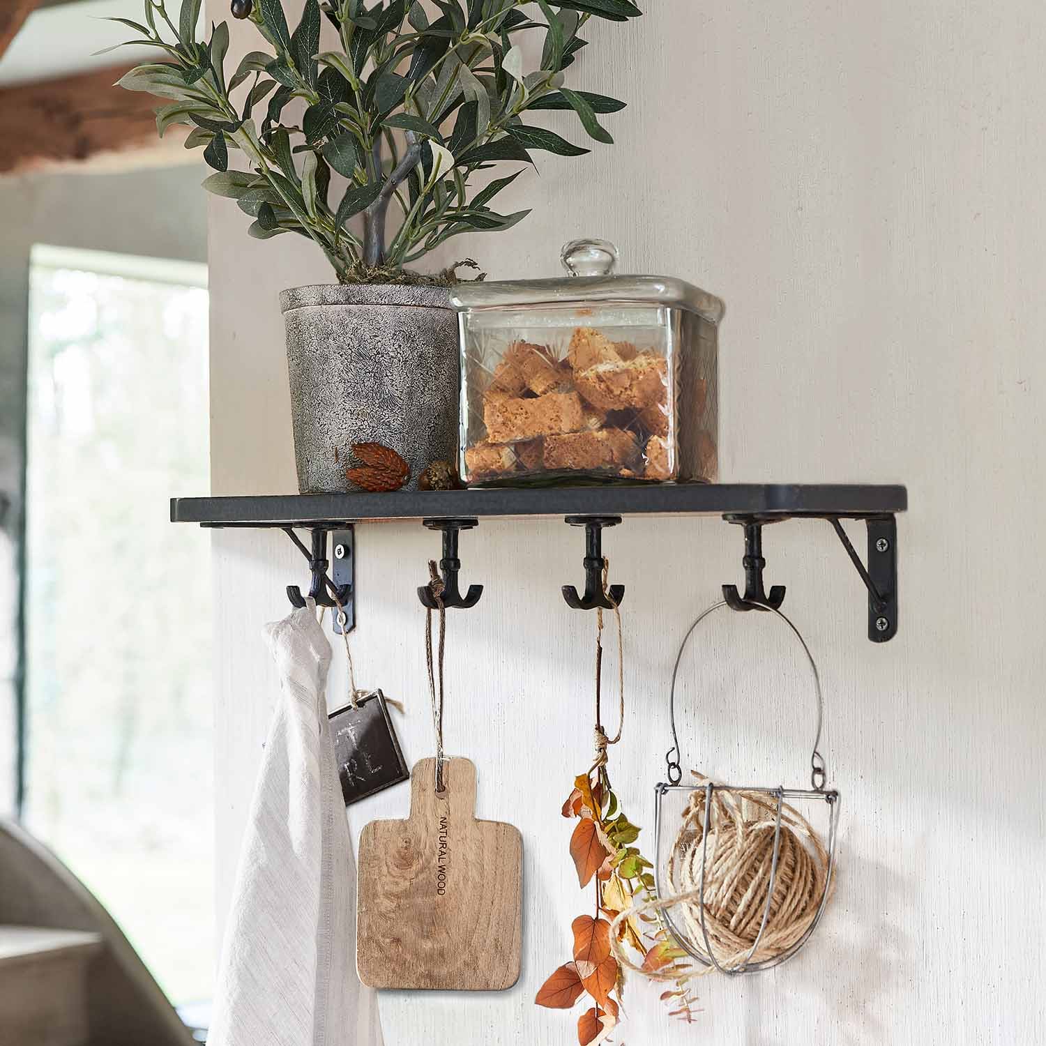 Estante de pared negro de metal con ganchos, planta en maceta y recipiente de vidrio con galletas