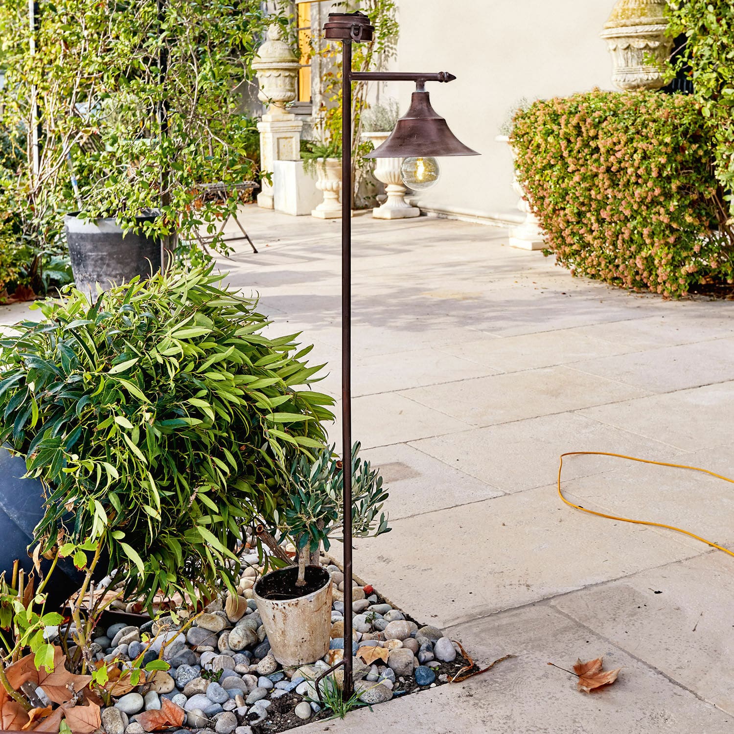 Farol solar Kaley Lámpara de jardín de metal color óxido con bombilla, sobre piedras entre plantas verdes