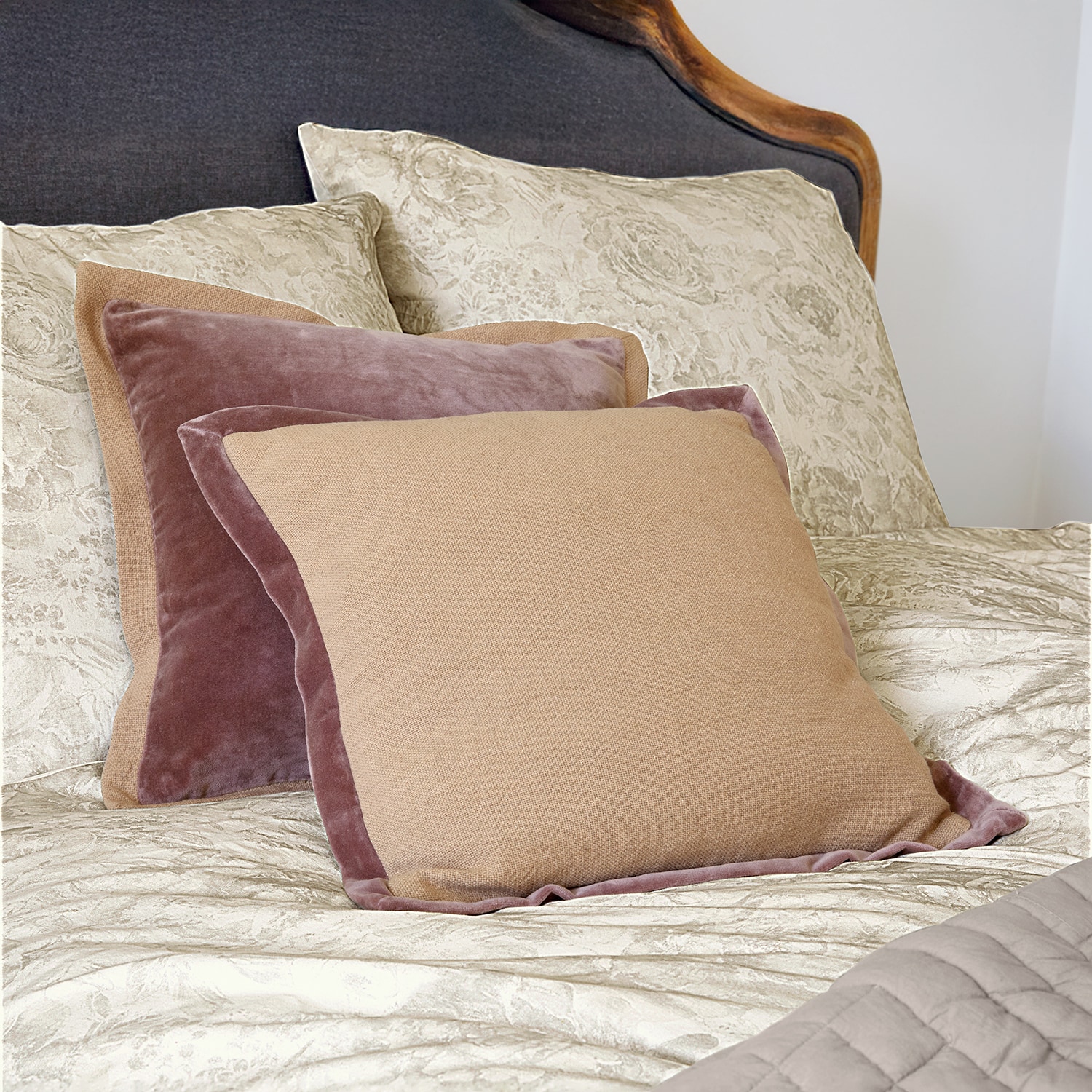 Cojines decorativos beige y rosa de terciopelo y tela sobre cama con ropa de cama clara