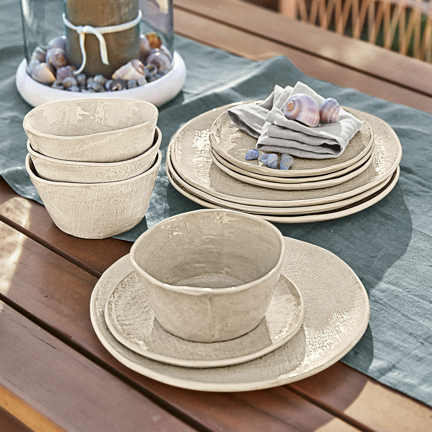 Vajilla de 12 piezas Luganville Juego de vajilla de cerámica beige sobre mesa de madera con conchas y mantel de lino