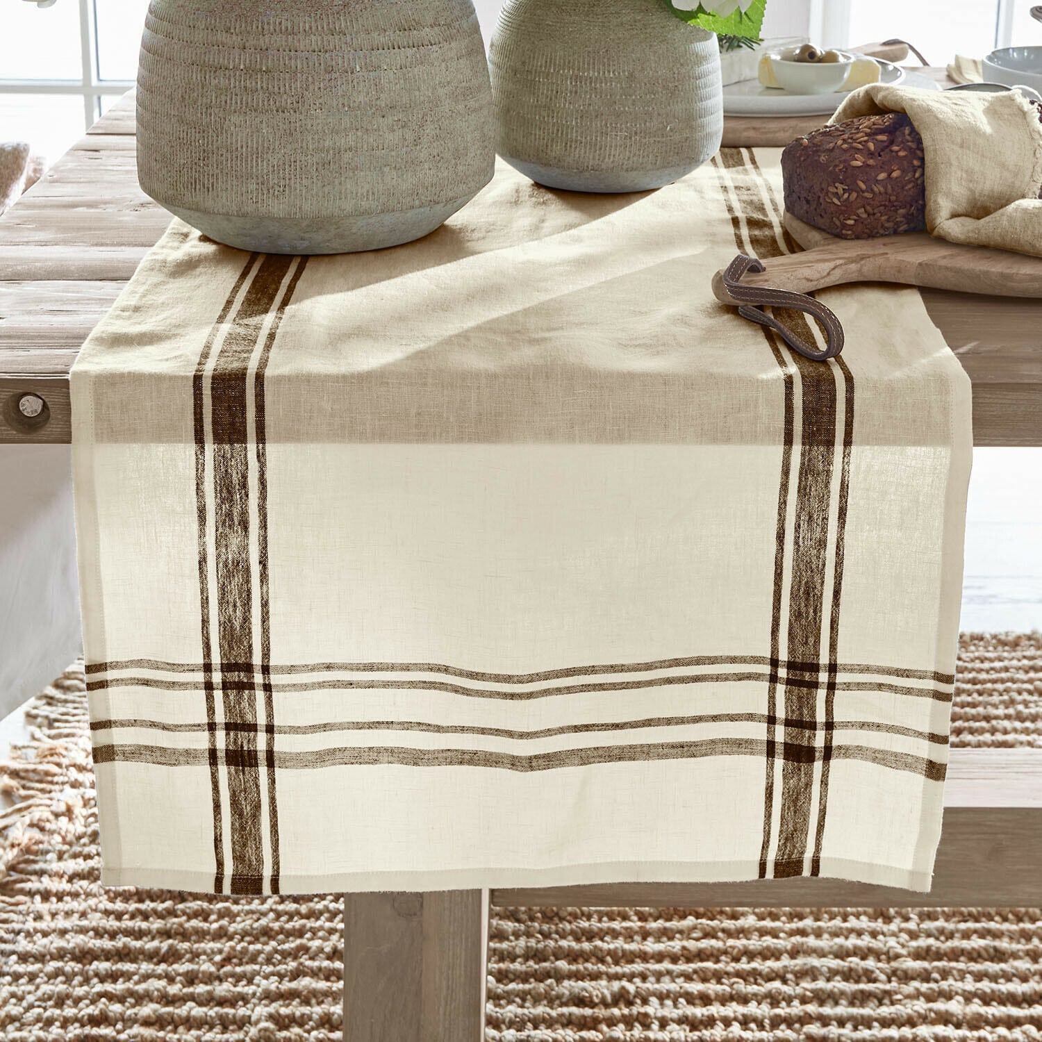 Camino de mesa Ellory Camino de mesa de lino beige con rayas marrones sobre mesa de madera, decoración con pan y vajilla