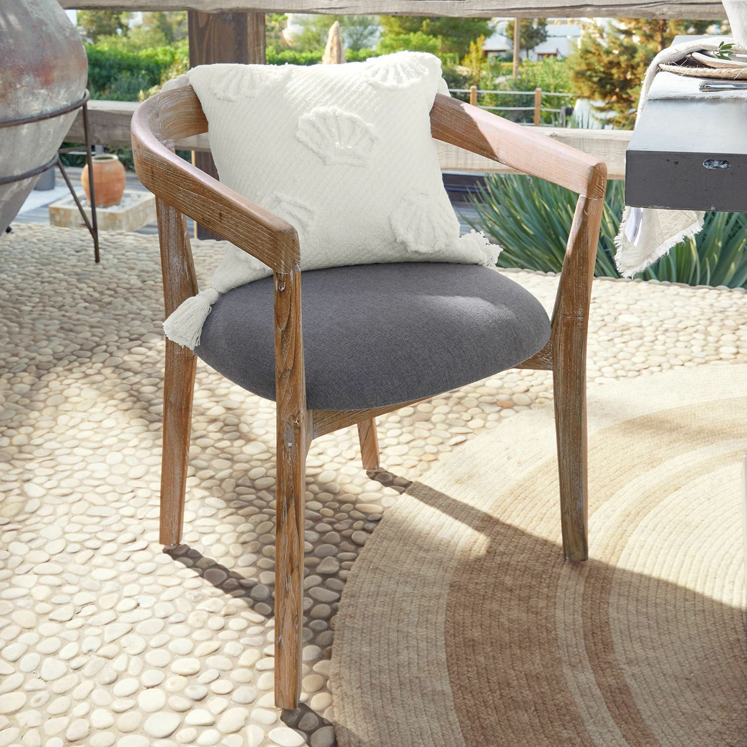 Silla Lunebois Silla de madera con asiento tapizado gris y cojín decorativo blanco en terraza soleada
