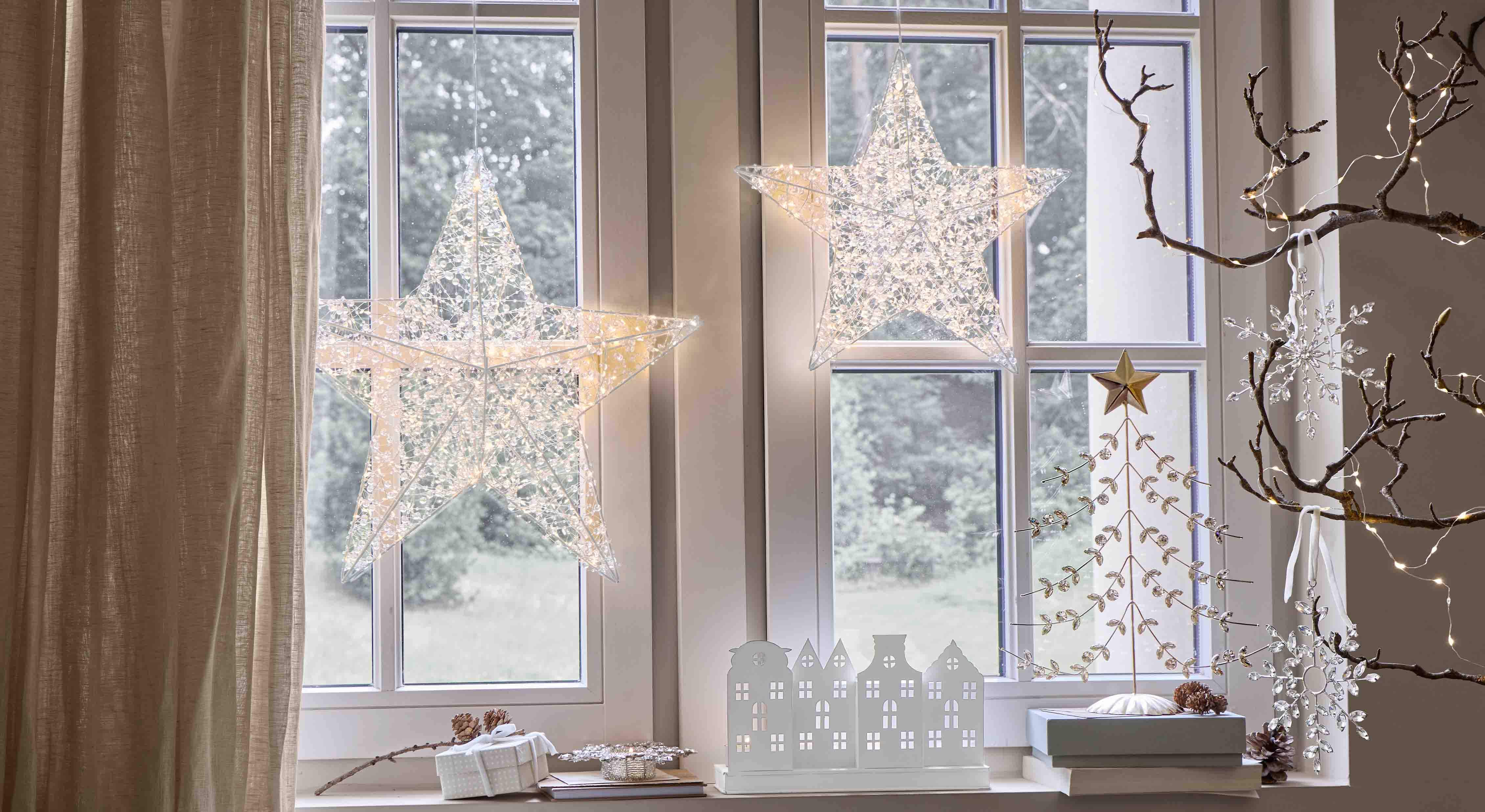 Estrellas decorativas luminosas de material transparente colgadas en la ventana, iluminación festiva interior