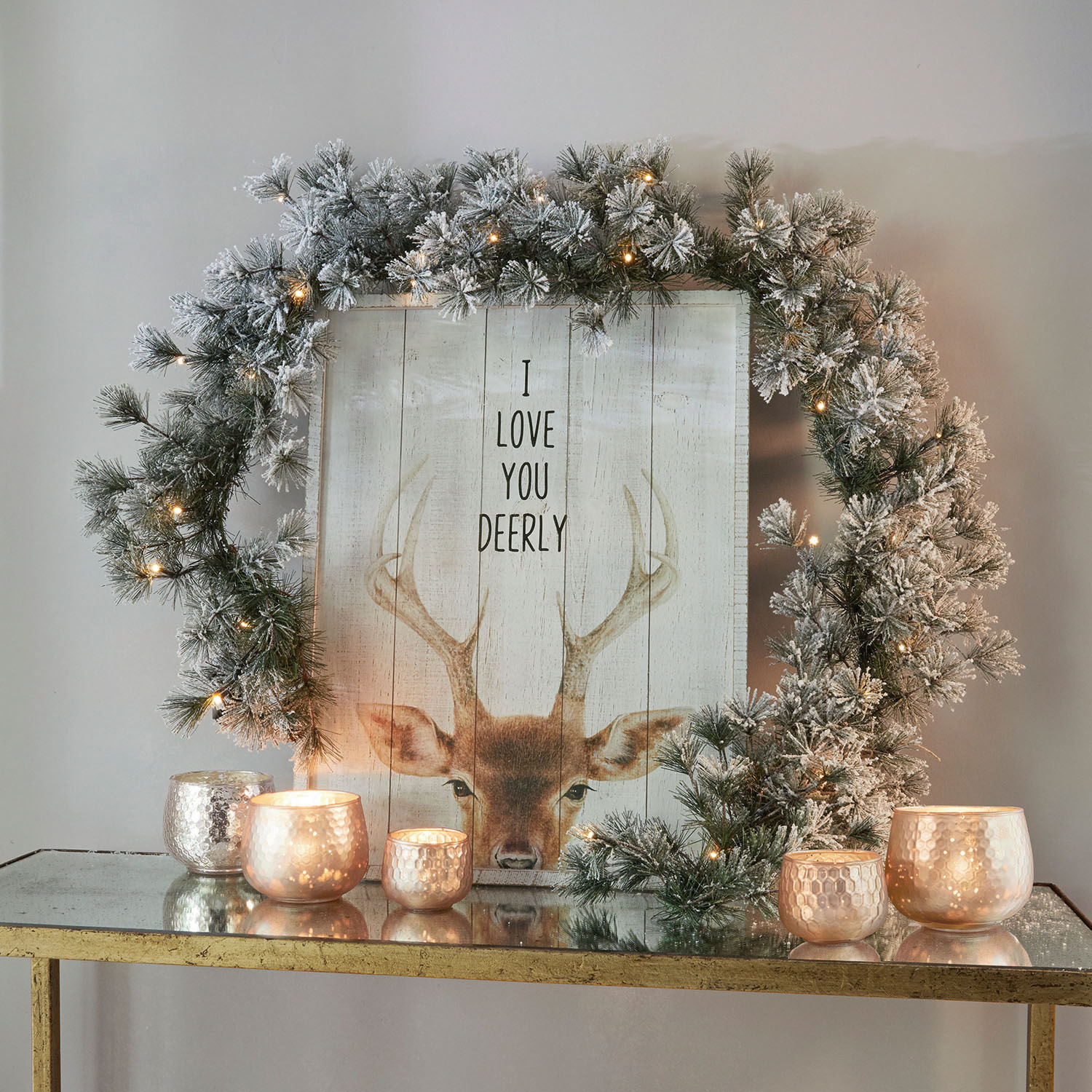 Guirnalda Toni Corona decorativa con ramas nevadas y luces LED sobre mesa dorada con velas encendidas