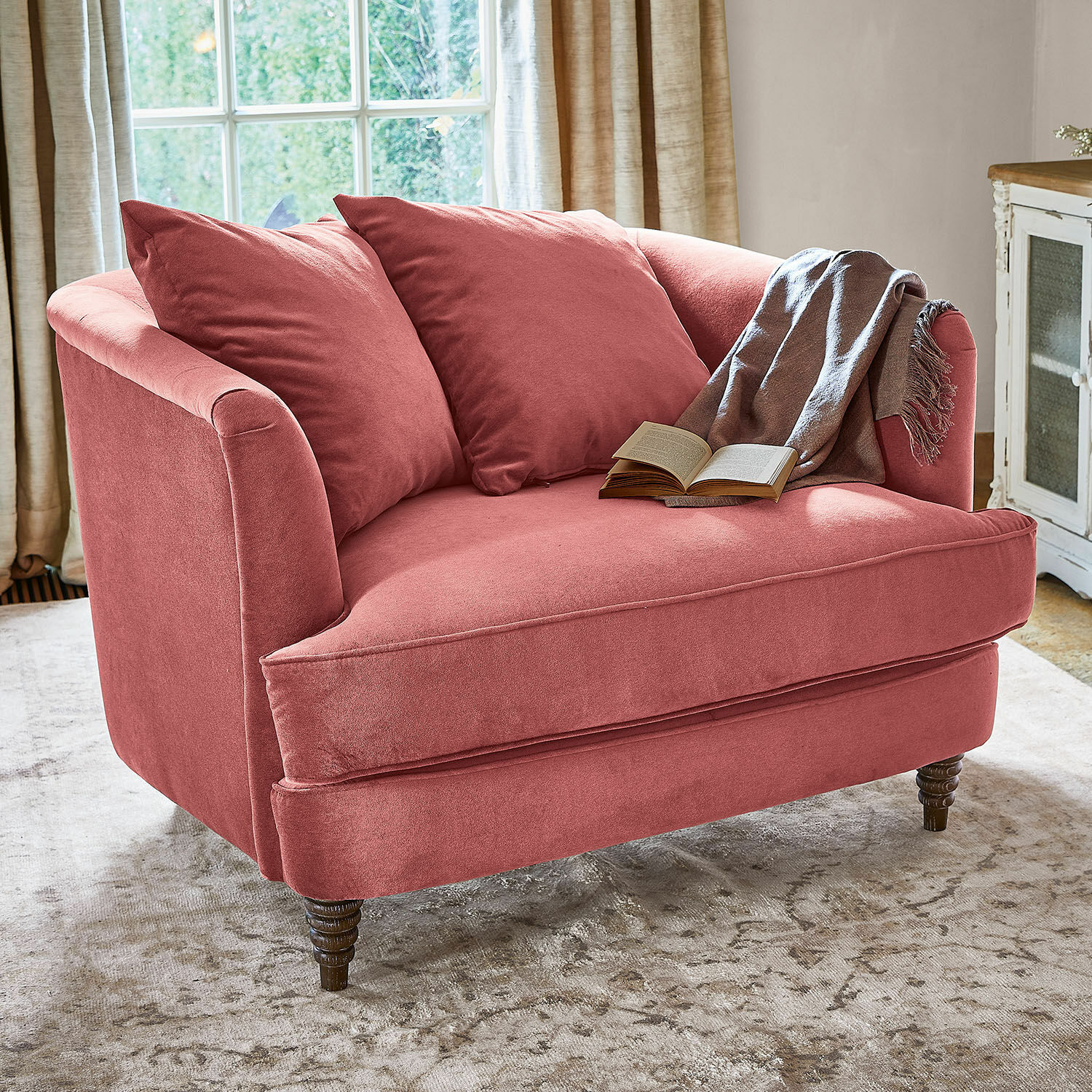 Sillón Etueffont Sofá rosa de tela suave con cojines y manta gris sobre alfombra clara en sala luminosa