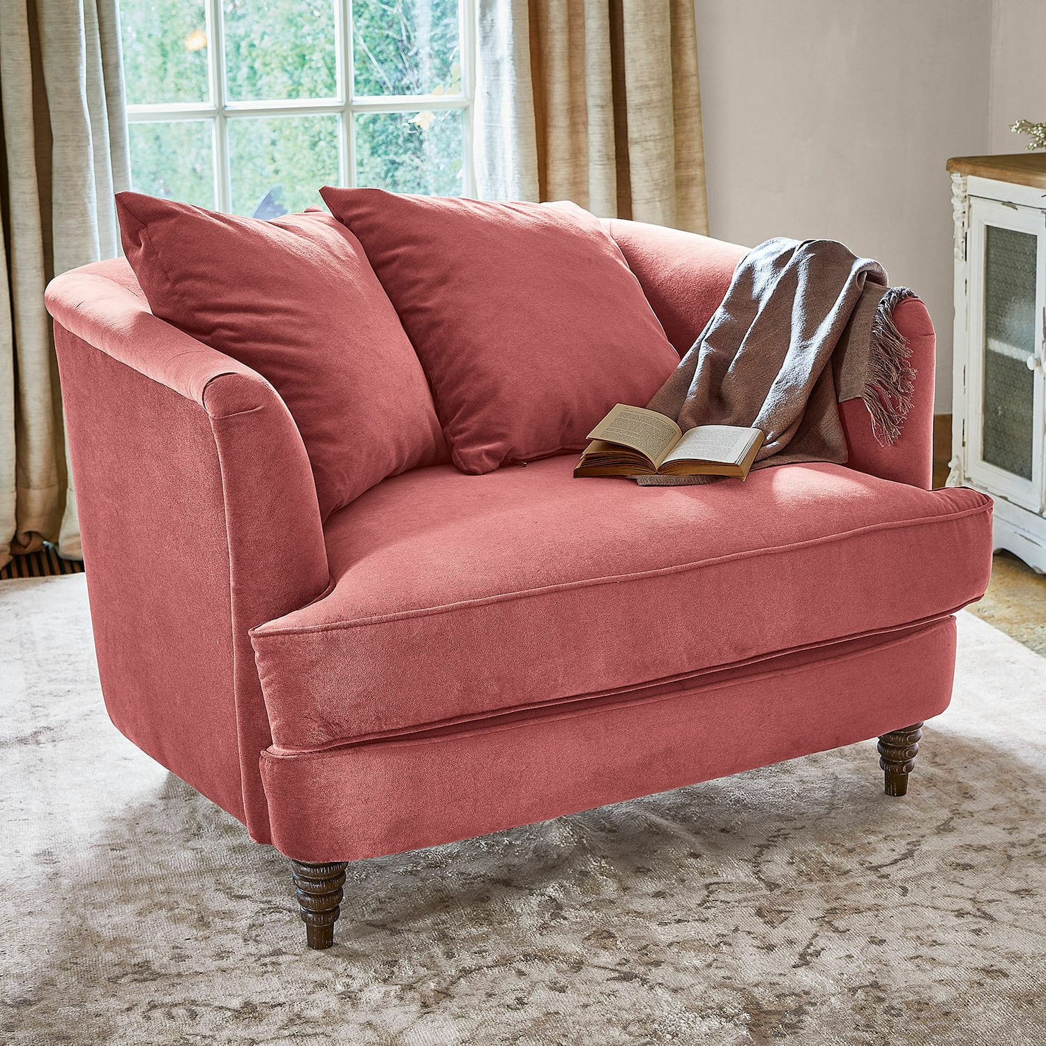 Sillón Etueffont Sofá rosa de tela suave con cojines y manta gris sobre alfombra clara en sala luminosa