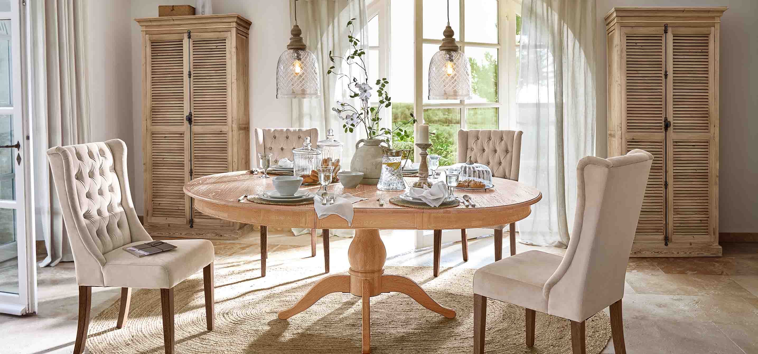 Comedor con mesa redonda de madera clara y sillas tapizadas beige en estilo vintage