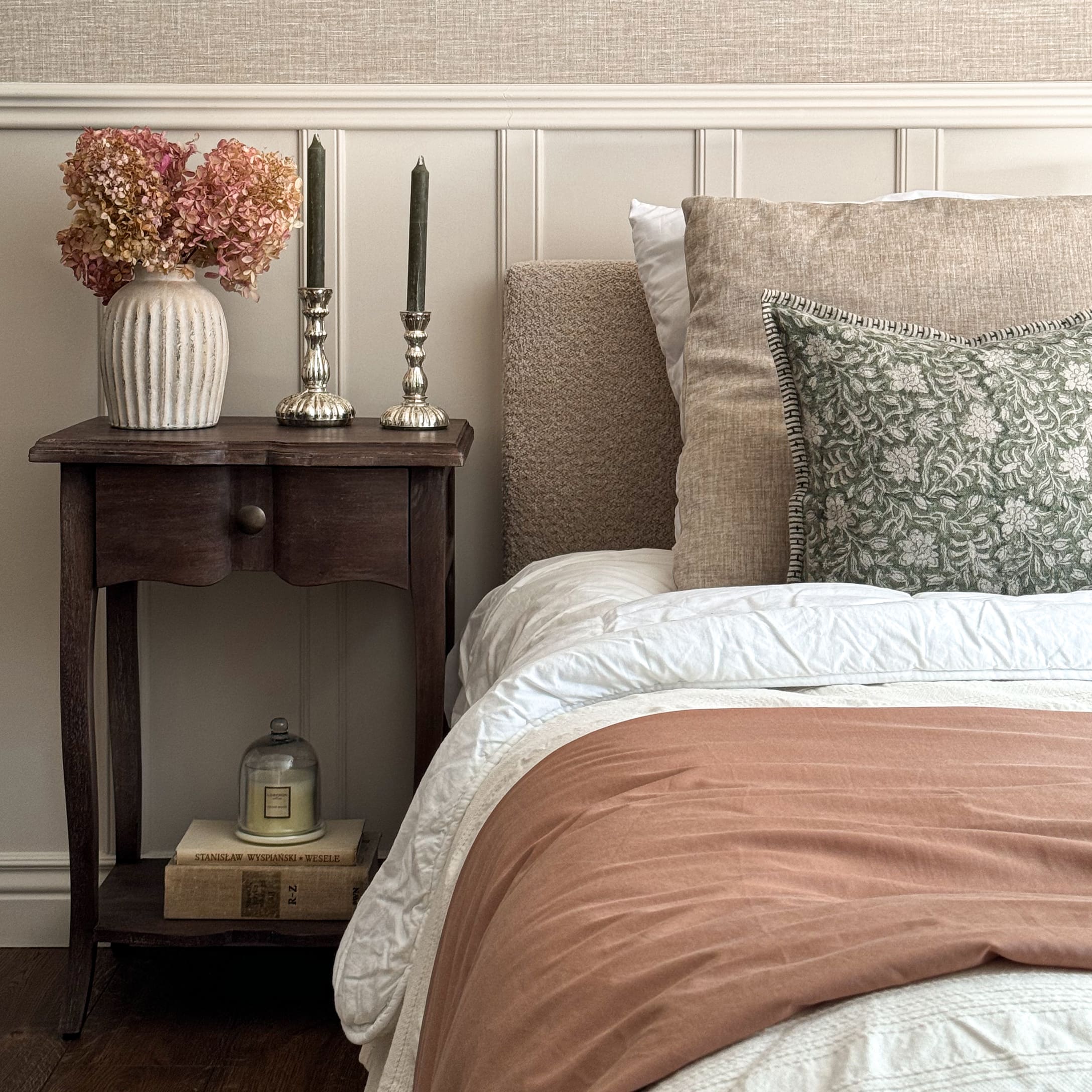 Dormitorio acogedor con ropa de cama beige, cojín verde y mesita de noche de madera con decoraciones