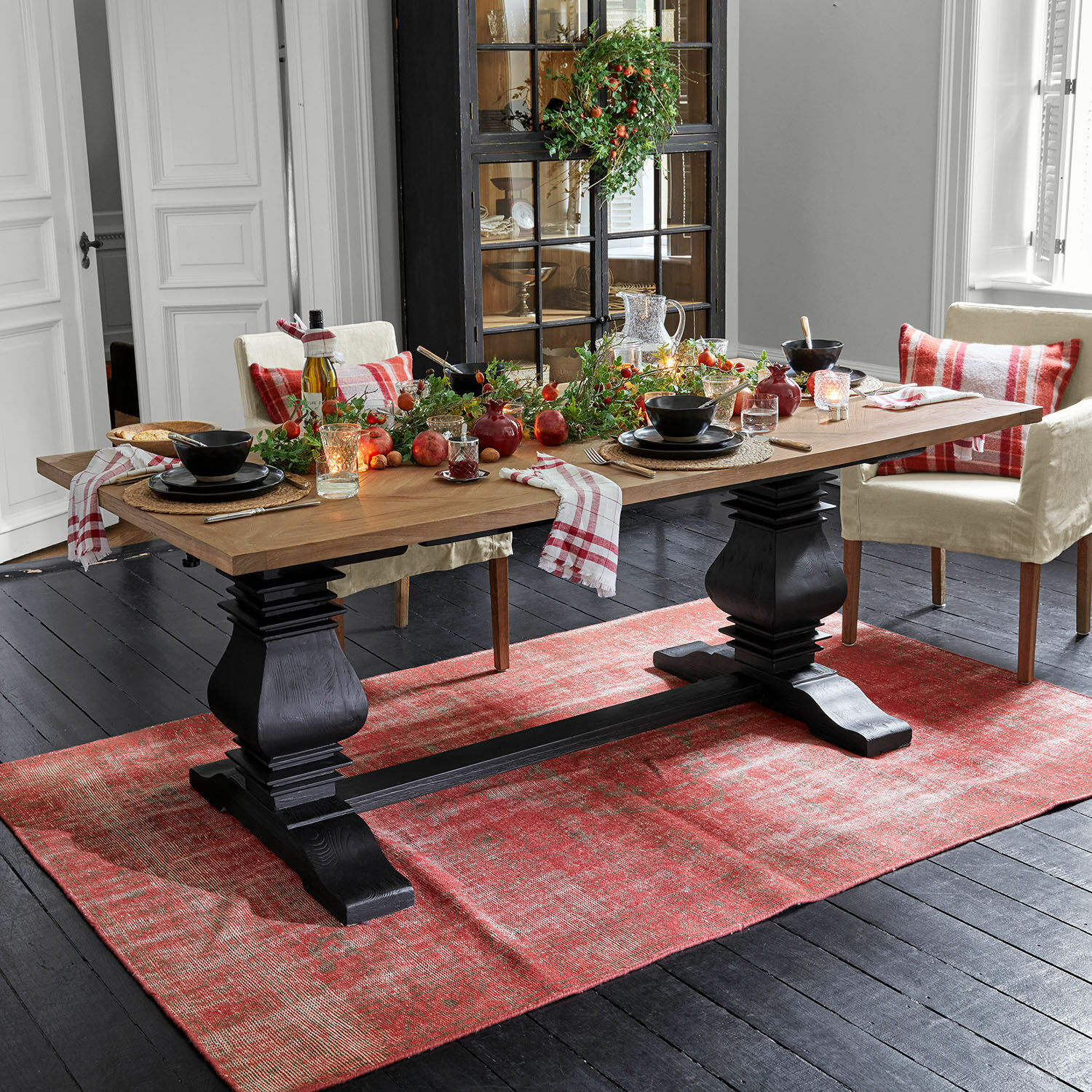 Mesa Quillancourt Mesa de comedor con tablero de madera y base negra sobre alfombra roja, decoración festiva