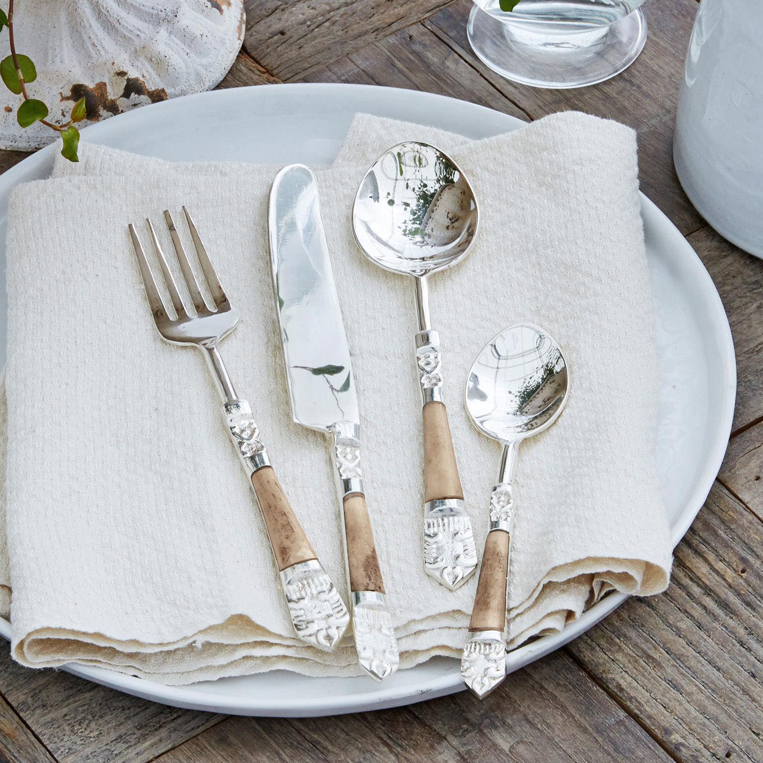 Set de 4 cubiertos Ferrette Juego de cubiertos con cabezas metálicas y mangos de madera sobre plato blanco con servilleta de lino