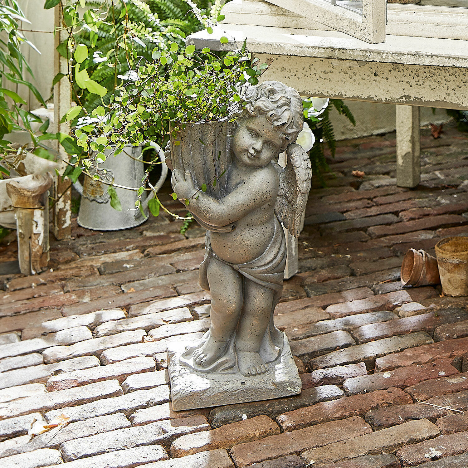 Jardinera Pirie Figura de ángel de piedra gris con maceta y planta verde sobre suelo de ladrillo