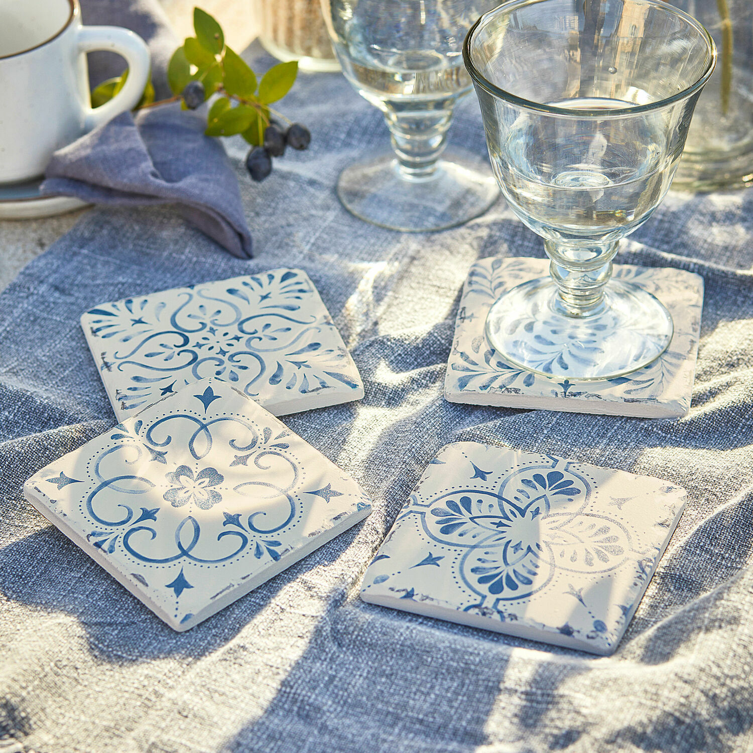 Set de 4 posavasos Évry Posavasos de cerámica blanca con diseño azul sobre mantel de lino azul