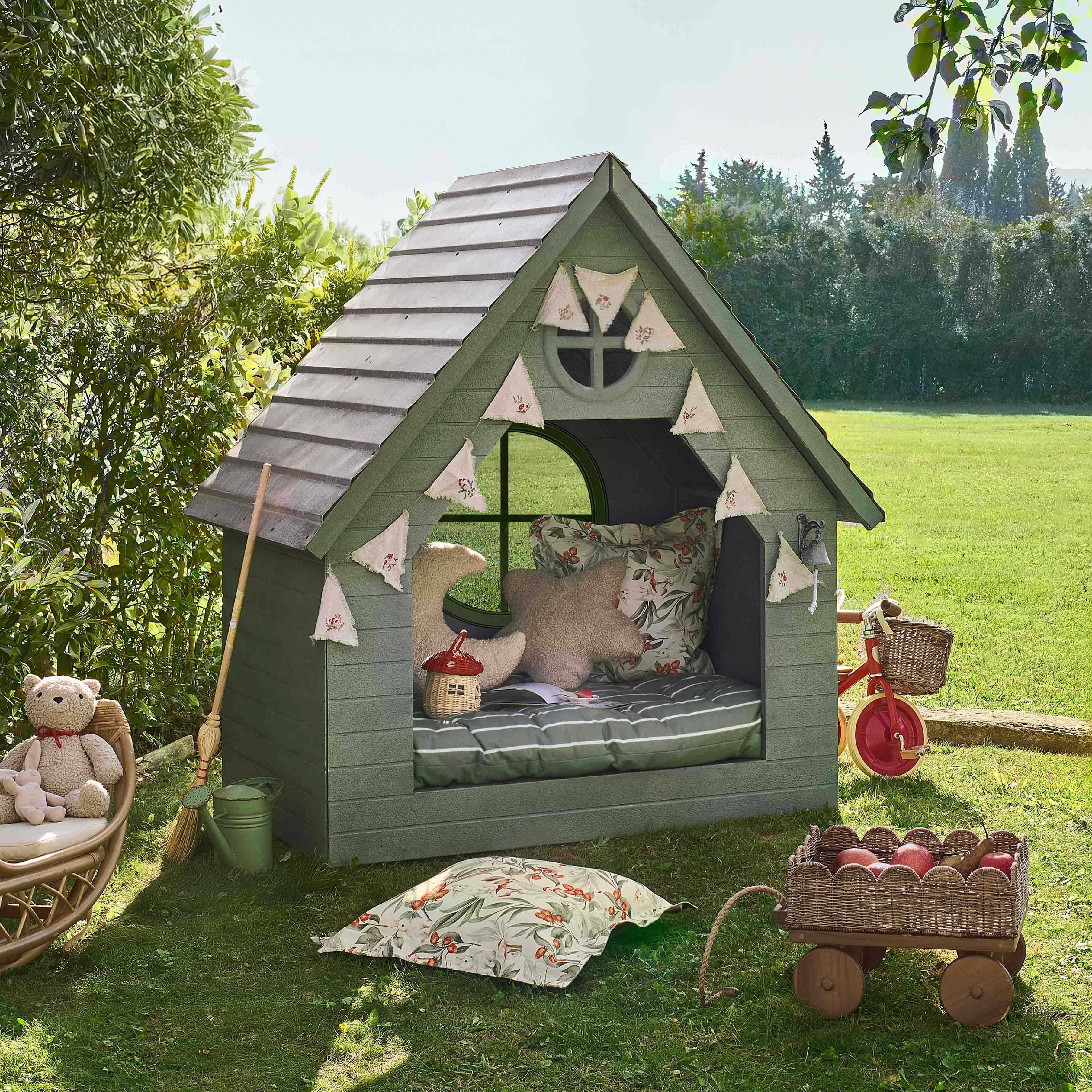 Casita de jardín verde de madera con cojines decorativos y guirnalda, ideal para juegos infantiles.