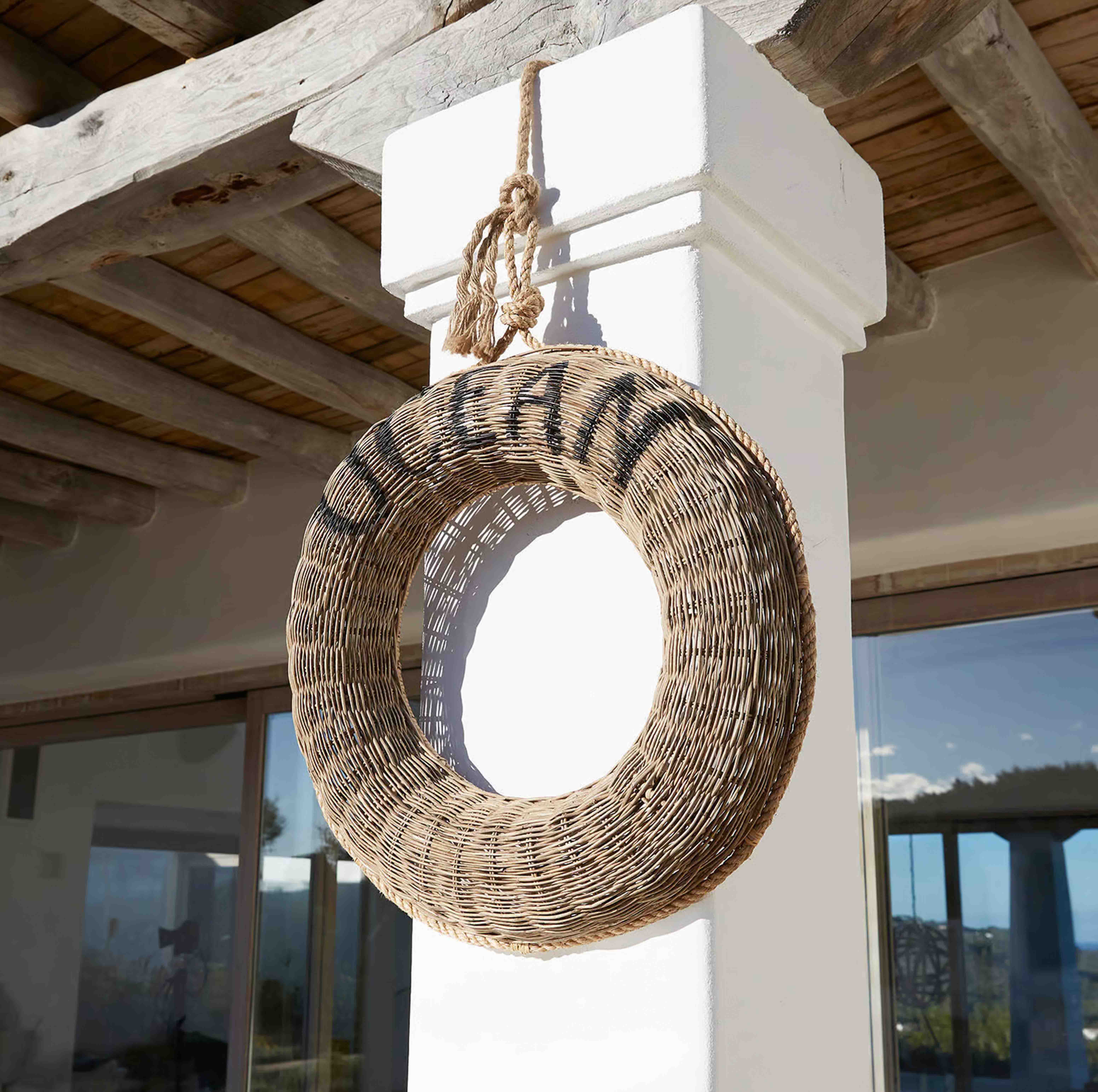 Corona redonda de mimbre natural colgada en una columna blanca bajo un techo de madera rústica