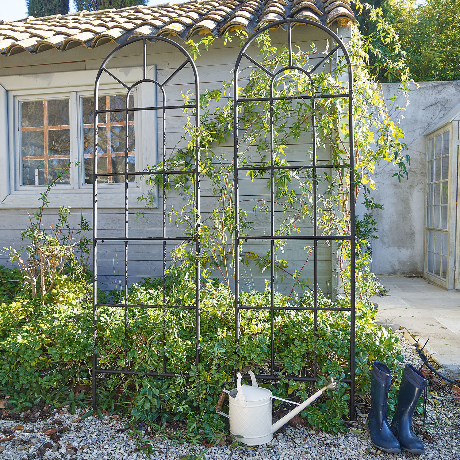 Set de 2 enrejados Ealdred Enrejado de jardín negro de metal con diseño arqueado frente a plantas y casa, regadera y botas azules