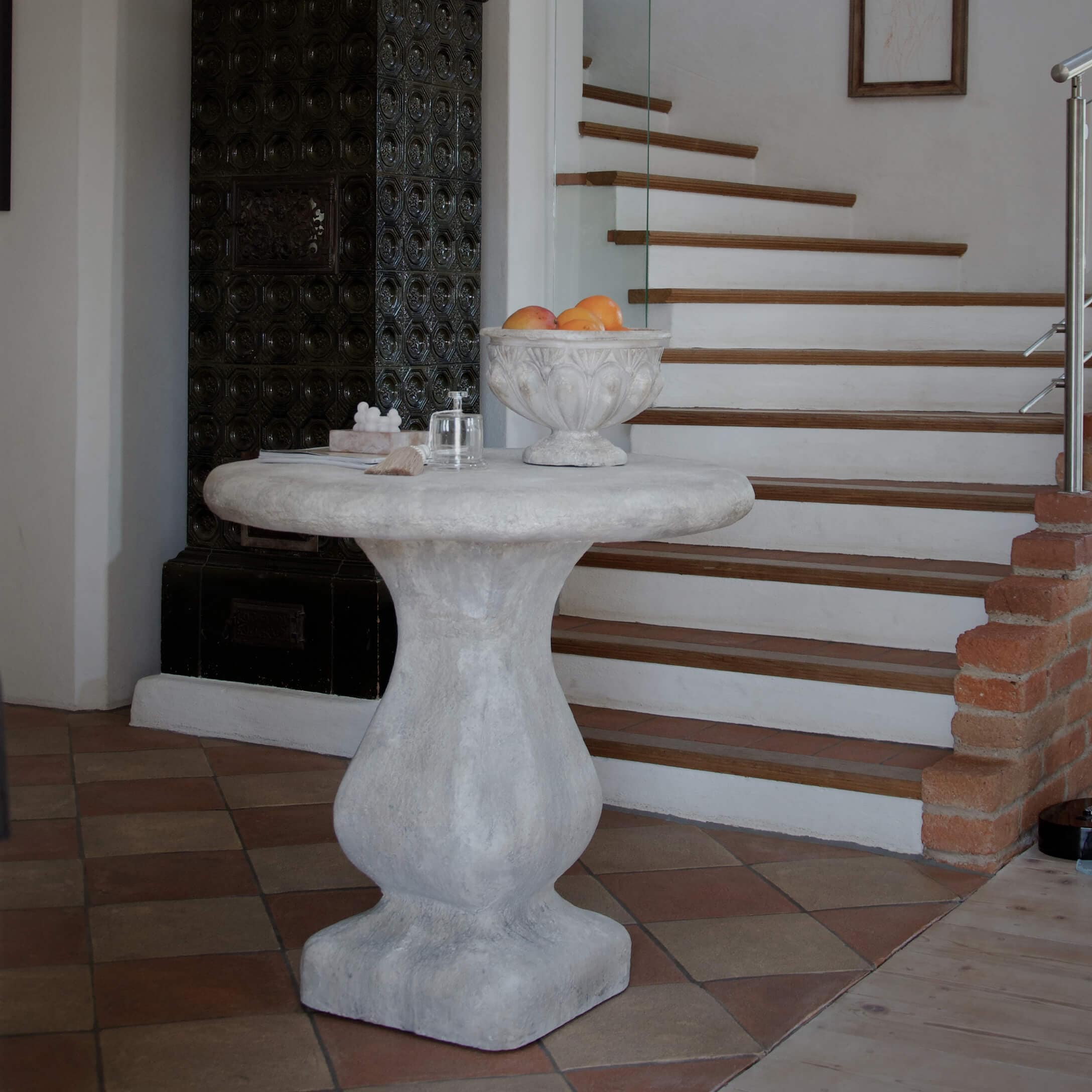 Mesa redonda de hormigón gris junto a escaleras, cuenco decorativo con frutas encima