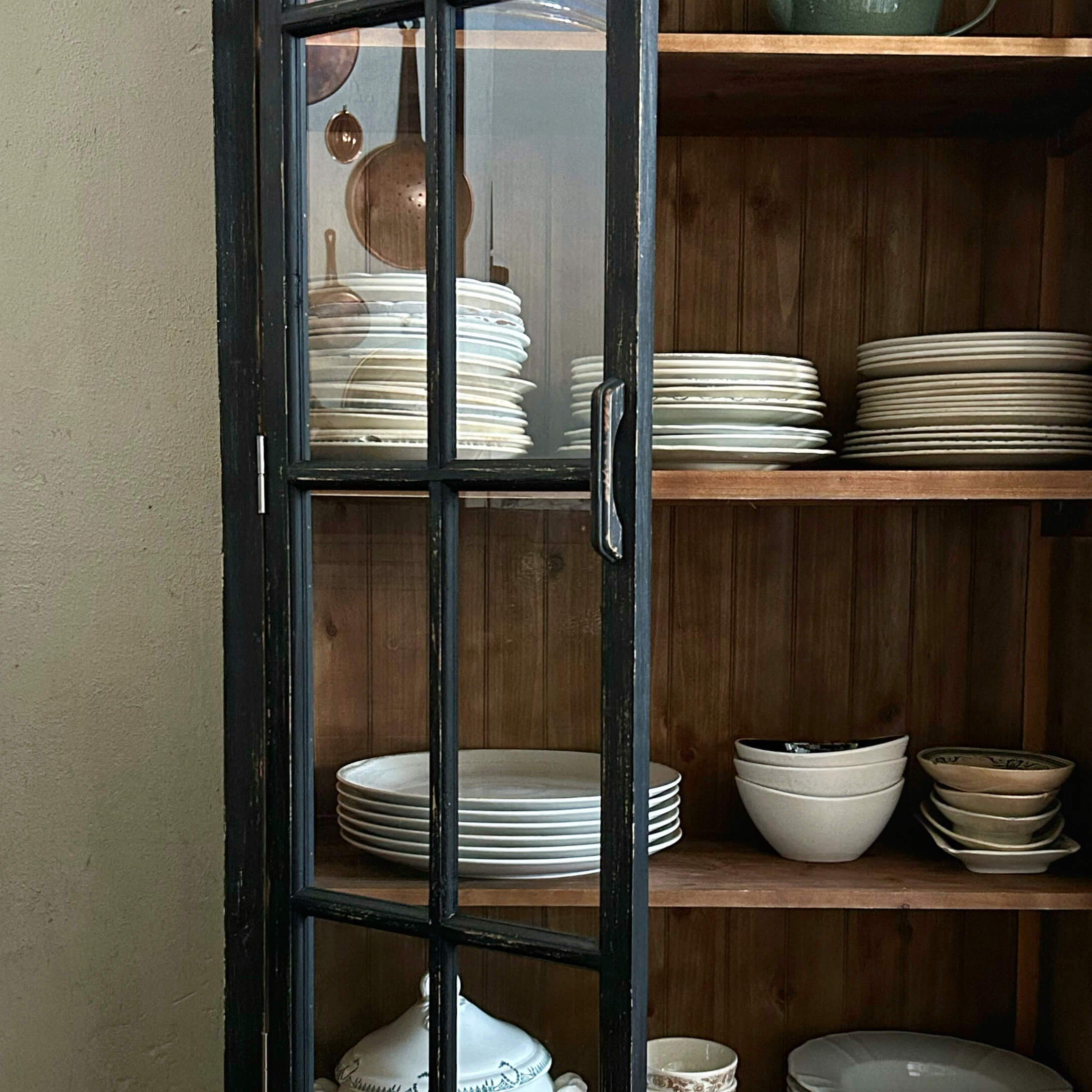 Puerta negra de madera con cristal de armario, dentro platos blancos y cuencos en estantes de madera