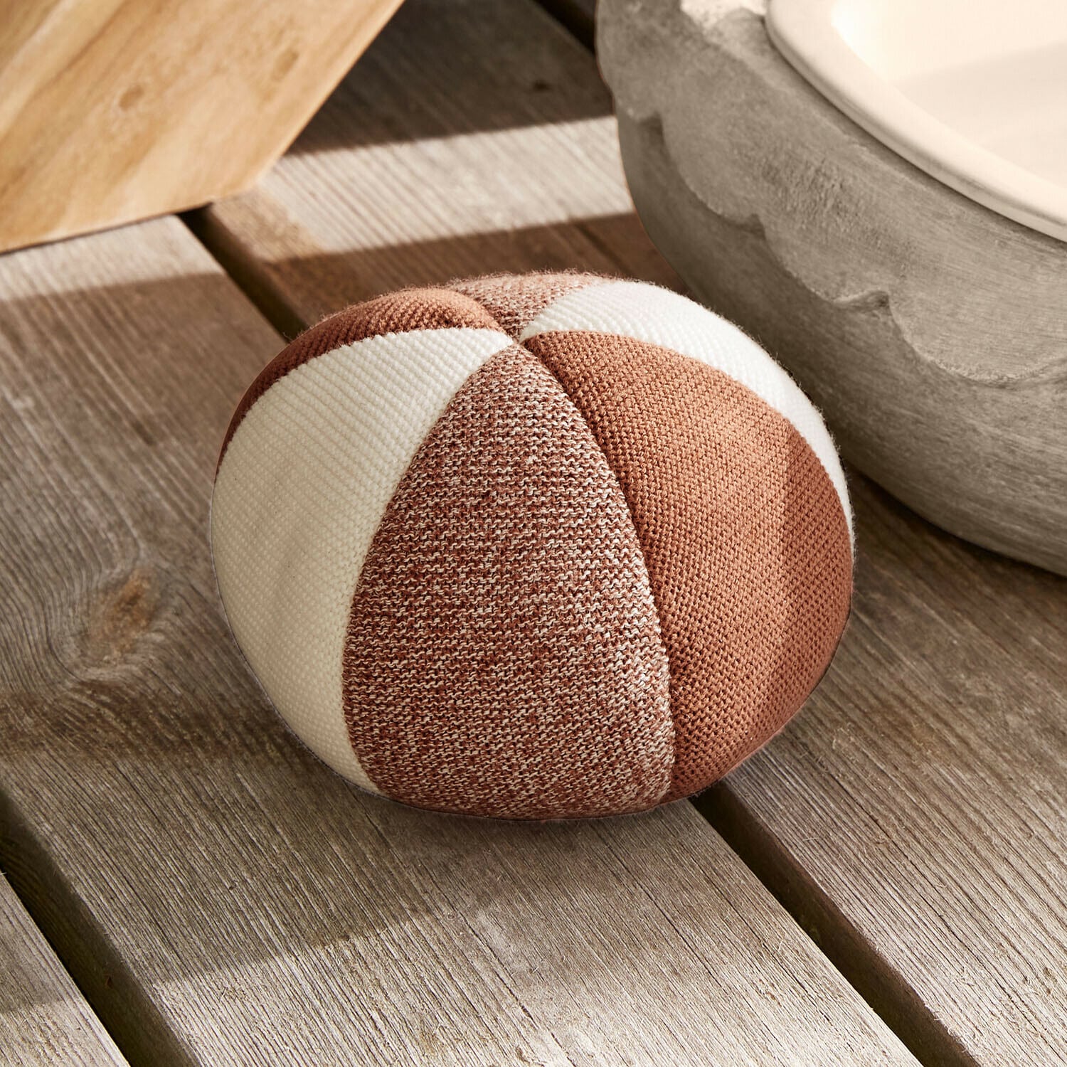 Cojín redondo de tela con rayas marrón y blanco sobre suelo de madera clara
