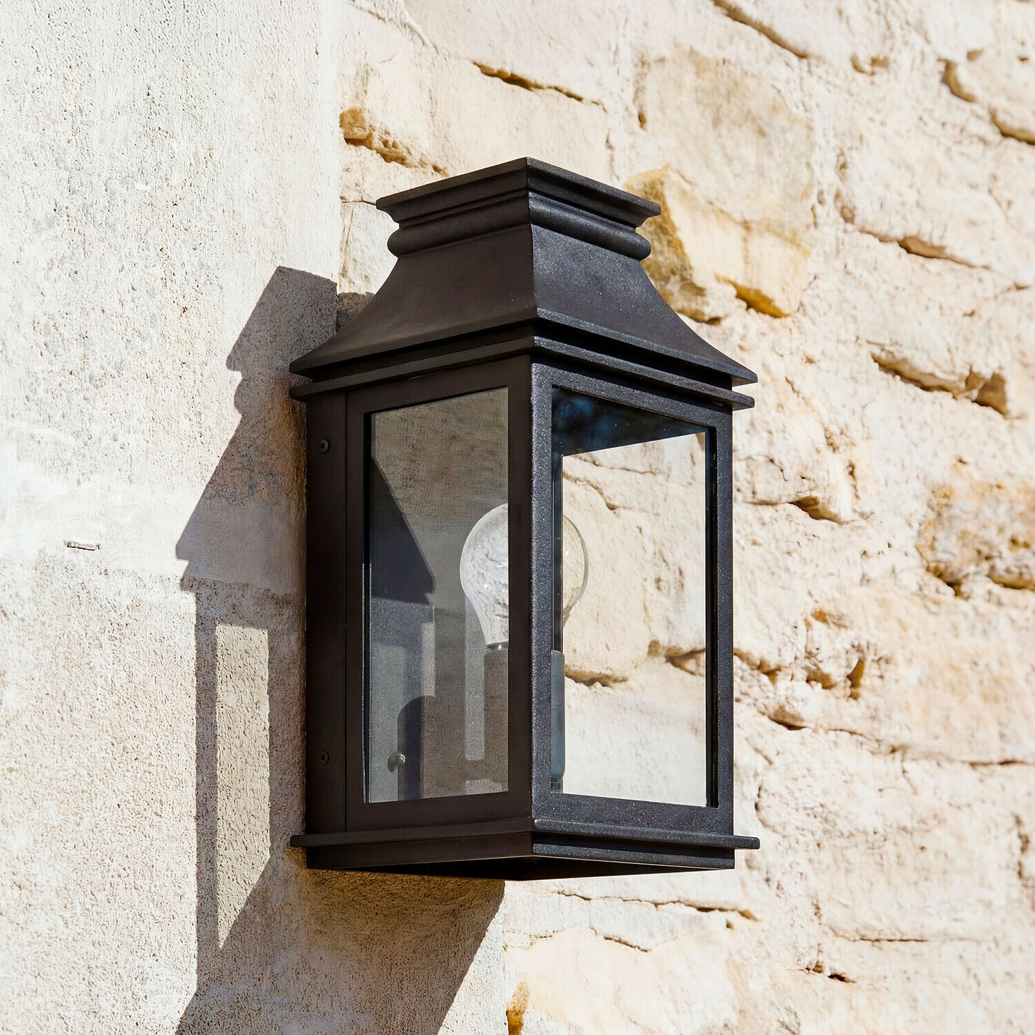 Lámpara de pared negra de metal con cristal transparente en pared de piedra clara, iluminación exterior